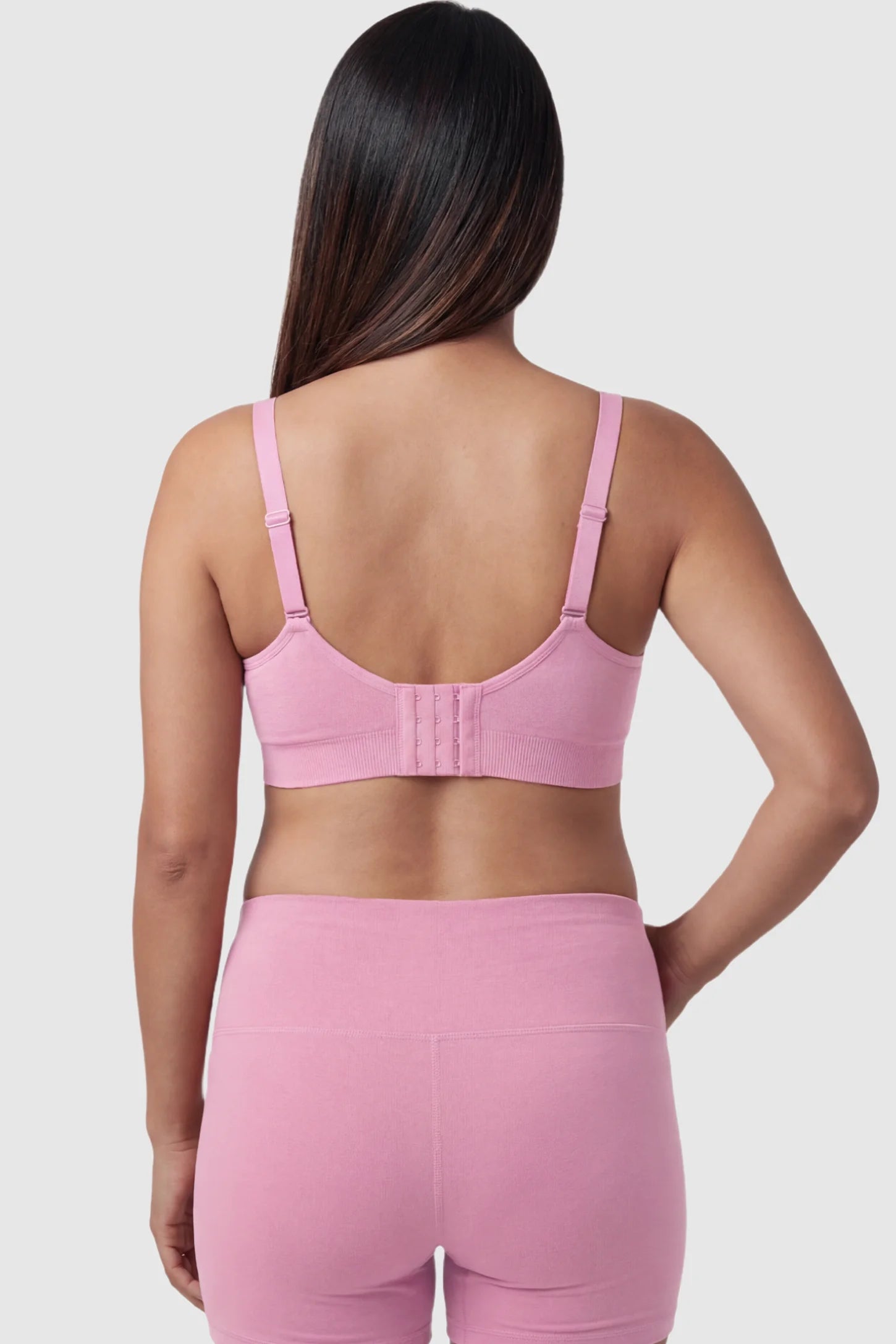 Seamless Ruched Front Maternity Nursing Bra Seamless Ruched Front Maternity Nursing Bra in peach pink featuring ribbed fabric, adjustable straps, and a multi-hook back closure on a pregnant model from behind.