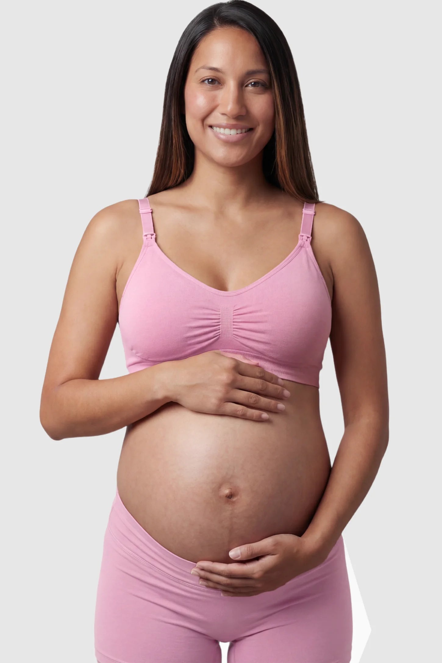 Seamless Ruched Front Maternity Nursing Bra Seamless Ruched Front Maternity Nursing Bra in peach pink featuring ribbed fabric and drop-down clips on a pregnant model showing front.