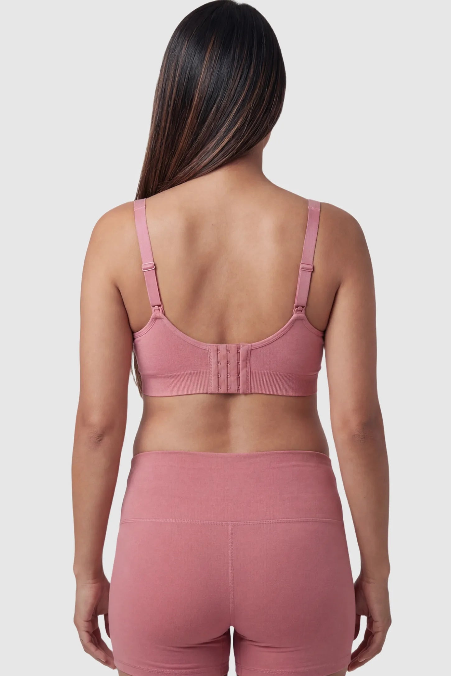 Seamless Ruched Front Maternity Nursing Bra Seamless Ruched Front Maternity Nursing Bra in pink featuring ribbed fabric, adjustable straps, and a multi-hook back closure on a pregnant model from behind.
