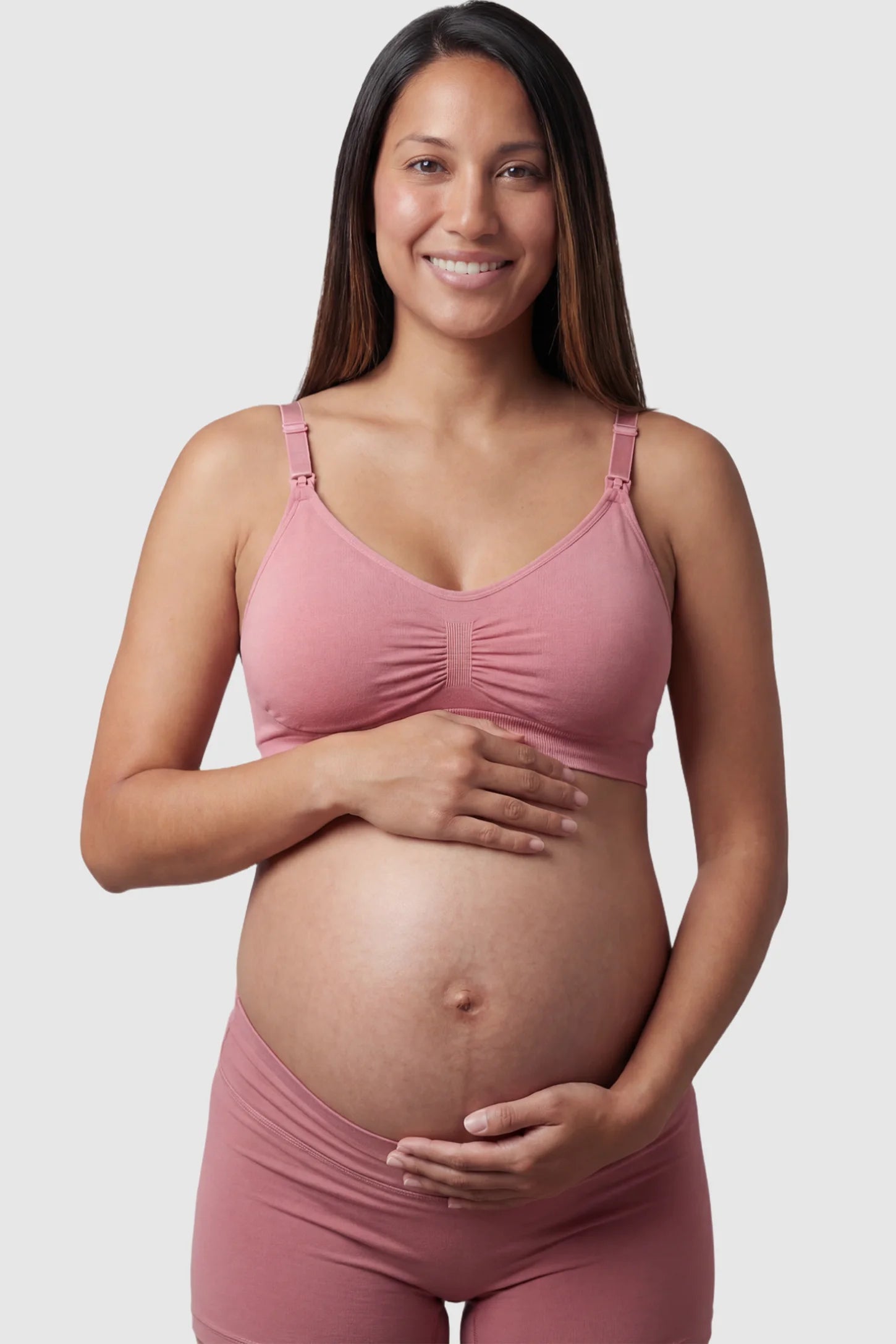 Seamless Ruched Front Maternity Nursing Bra Seamless Ruched Front Maternity Nursing Bra in pink featuring ribbed fabric and drop-down clips on a pregnant model showing front.