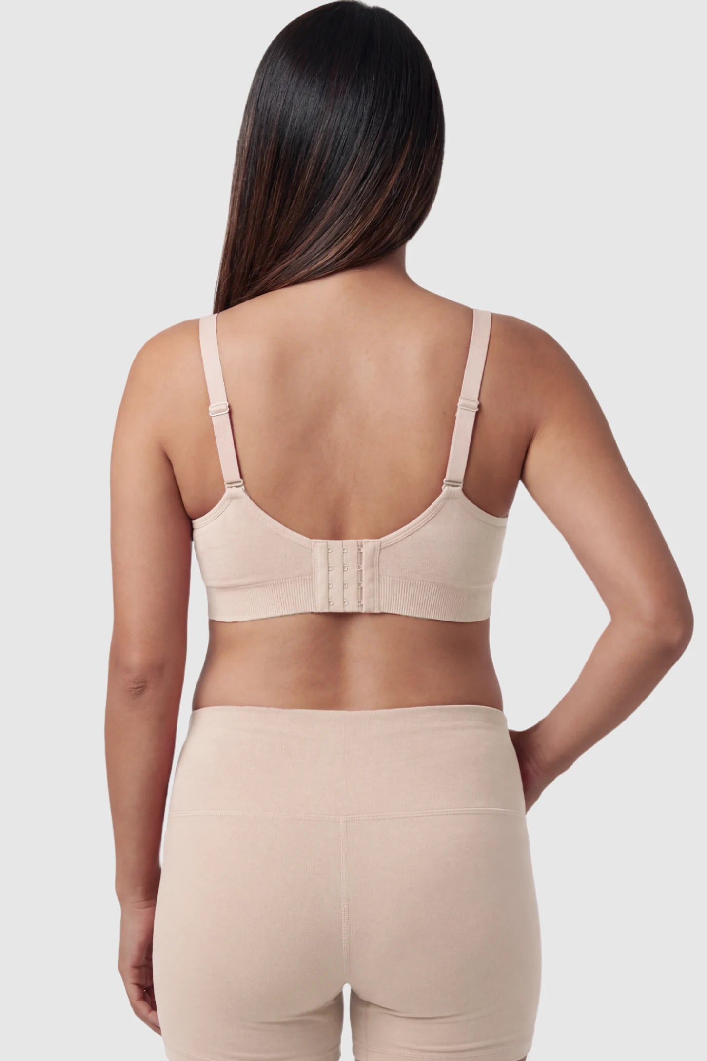 Seamless Ruched Front Maternity Nursing Bra Seamless Ruched Front Maternity Nursing Bra in skin featuring ribbed fabric, adjustable straps, and a multi-hook back closure on a pregnant model from behind.