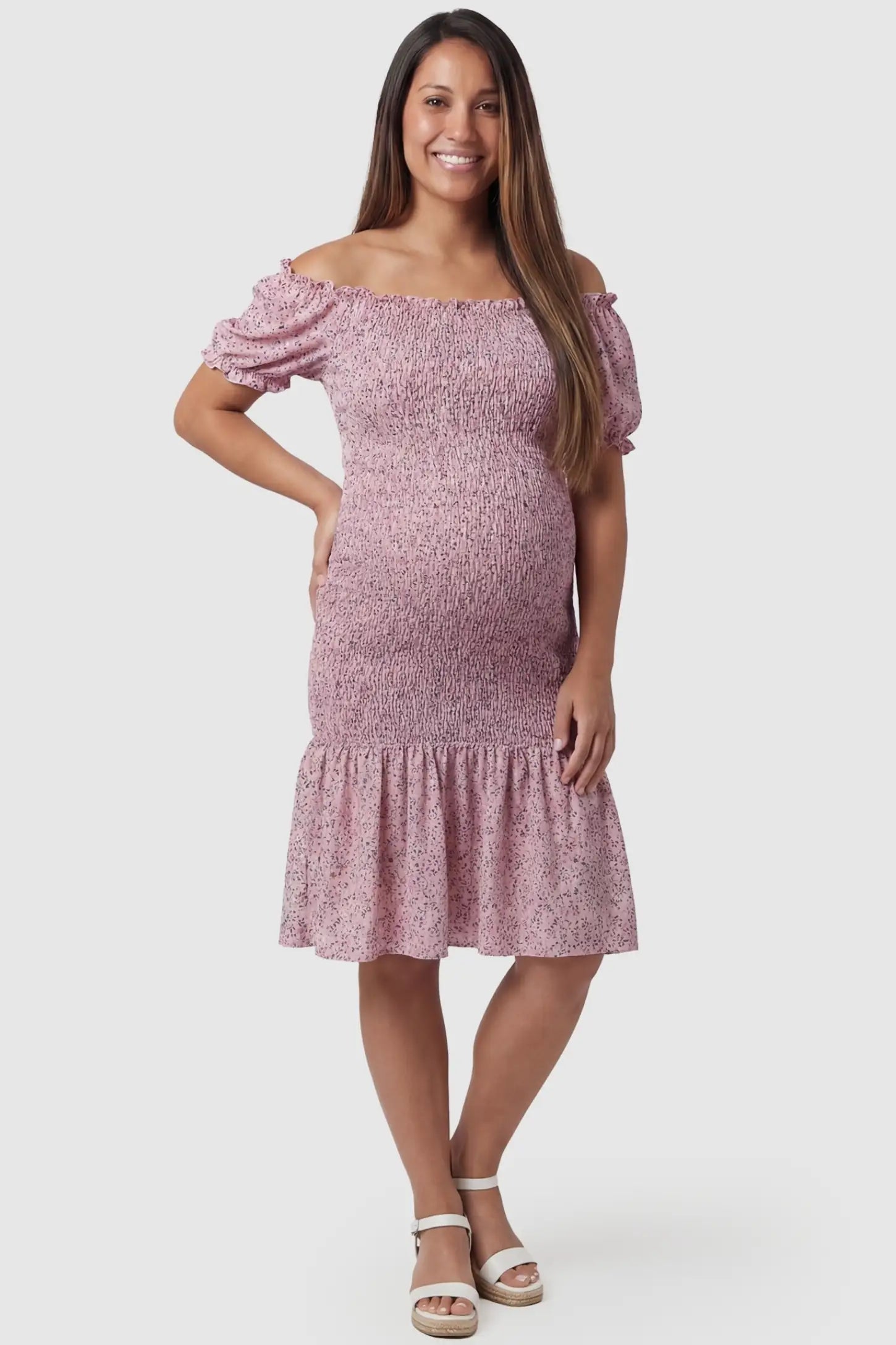 Floral Off Shoulder Smocked Maternity Fishtail Dress in Pink Floral featuring a ruffled neckline on a front-facing pregnant model.