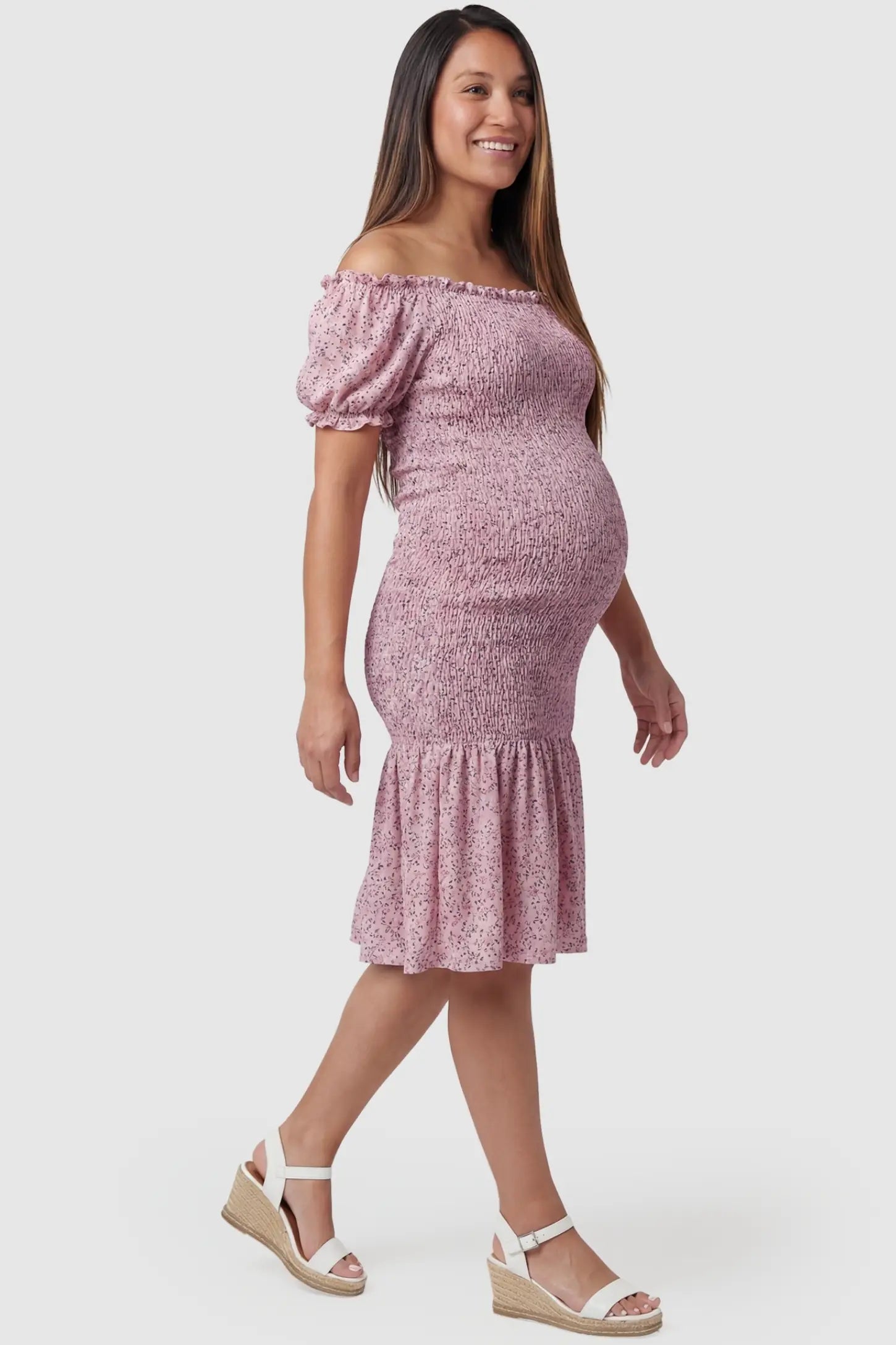 Floral Off Shoulder Smocked Maternity Fishtail Dress in Pink Floral featuring a curve-hugging silhouette on a side-profile pregnant model.