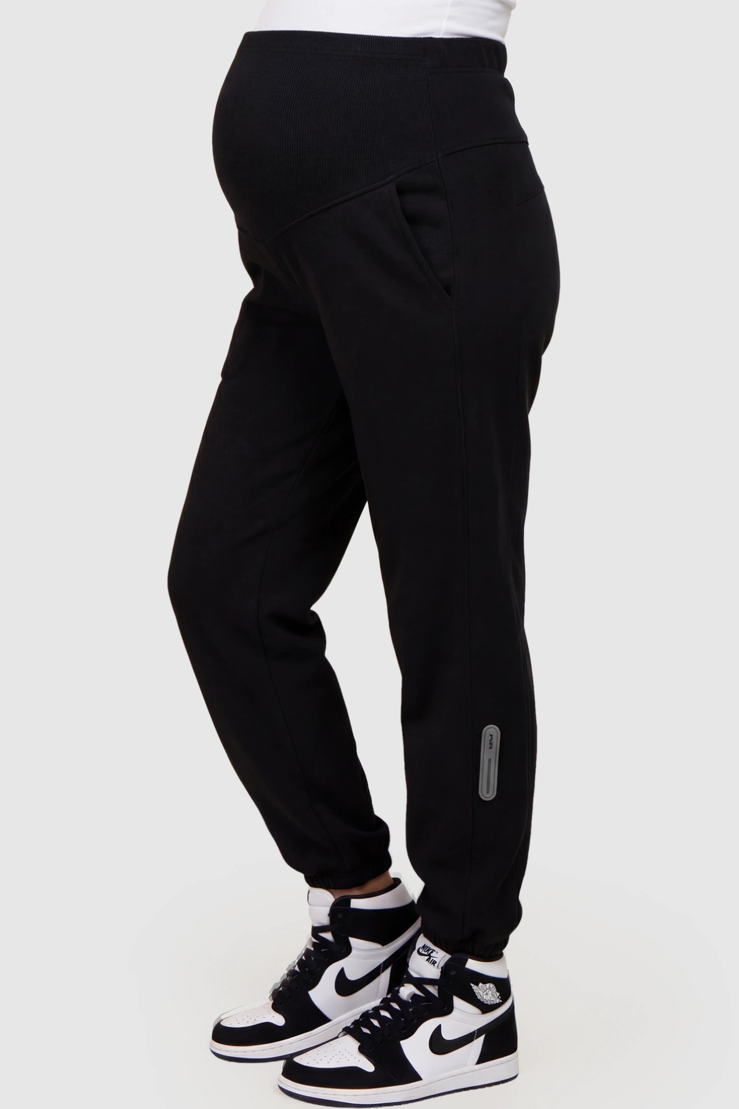 Cotton Blend Full Panel Tapered Leg Maternity Joggers Cotton Blend Full Panel Tapered Leg Maternity Joggers in Black featuring a high-waisted support band on a pregnant model showing side.