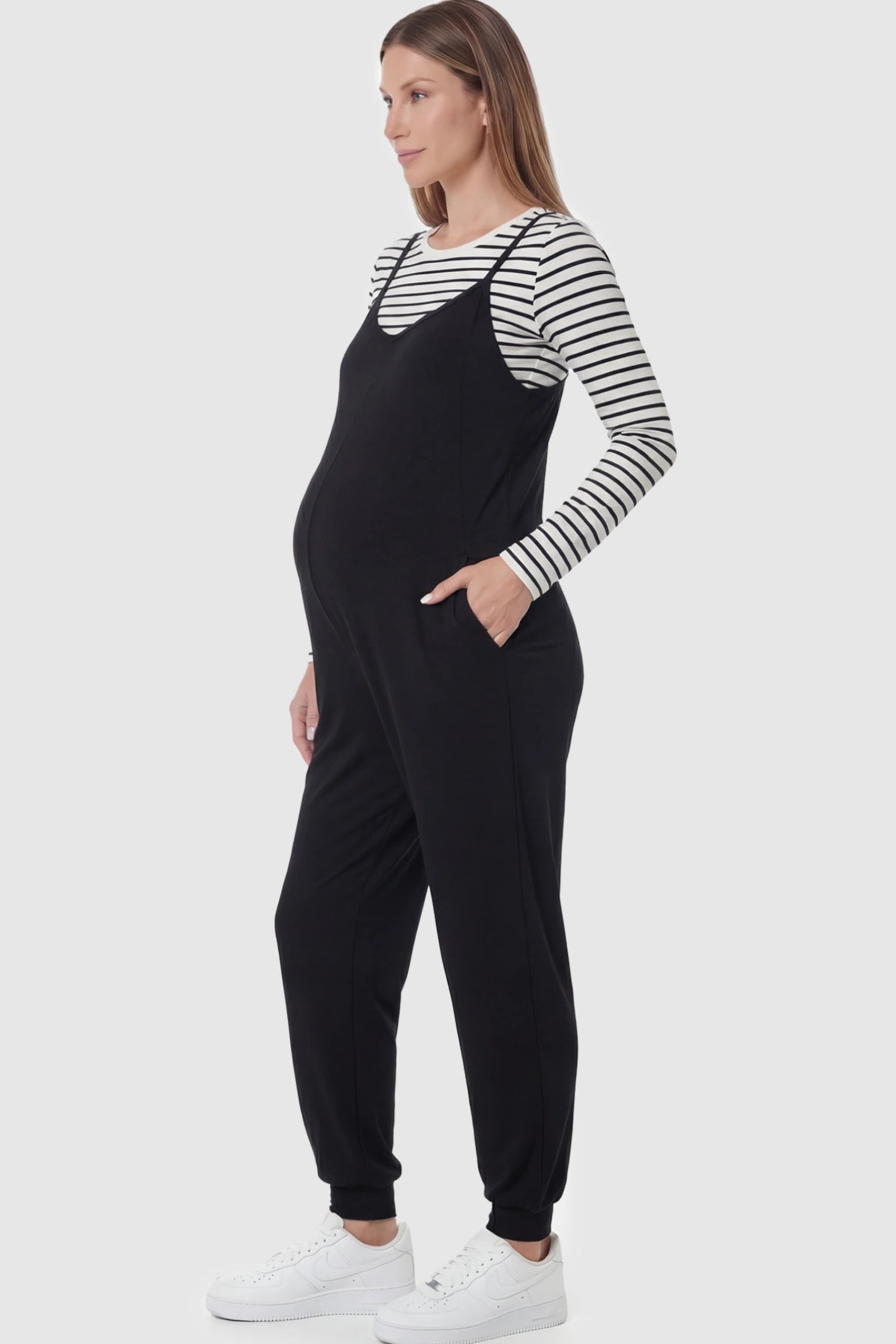 V-Neck Pocketed Maternity Jogger Jumpsuit V-Neck Pocketed Maternity Jogger Jumpsuit in Black featuring cotton-spandex jersey and side pockets on a pregnant model.