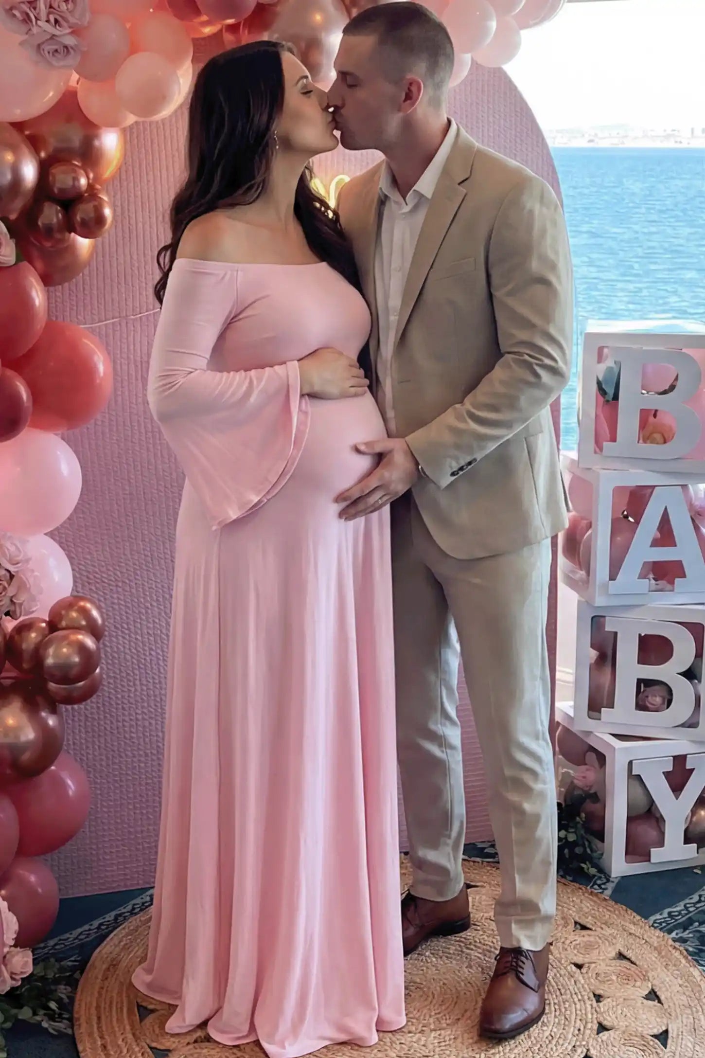 Solid Off Shoulder Bell Sleeve Maternity Maxi Dress Solid Off Shoulder Bell Sleeve Maternity Maxi Dress in Pink featuring Bell sleeves on a pregnant model posing with a partner.
