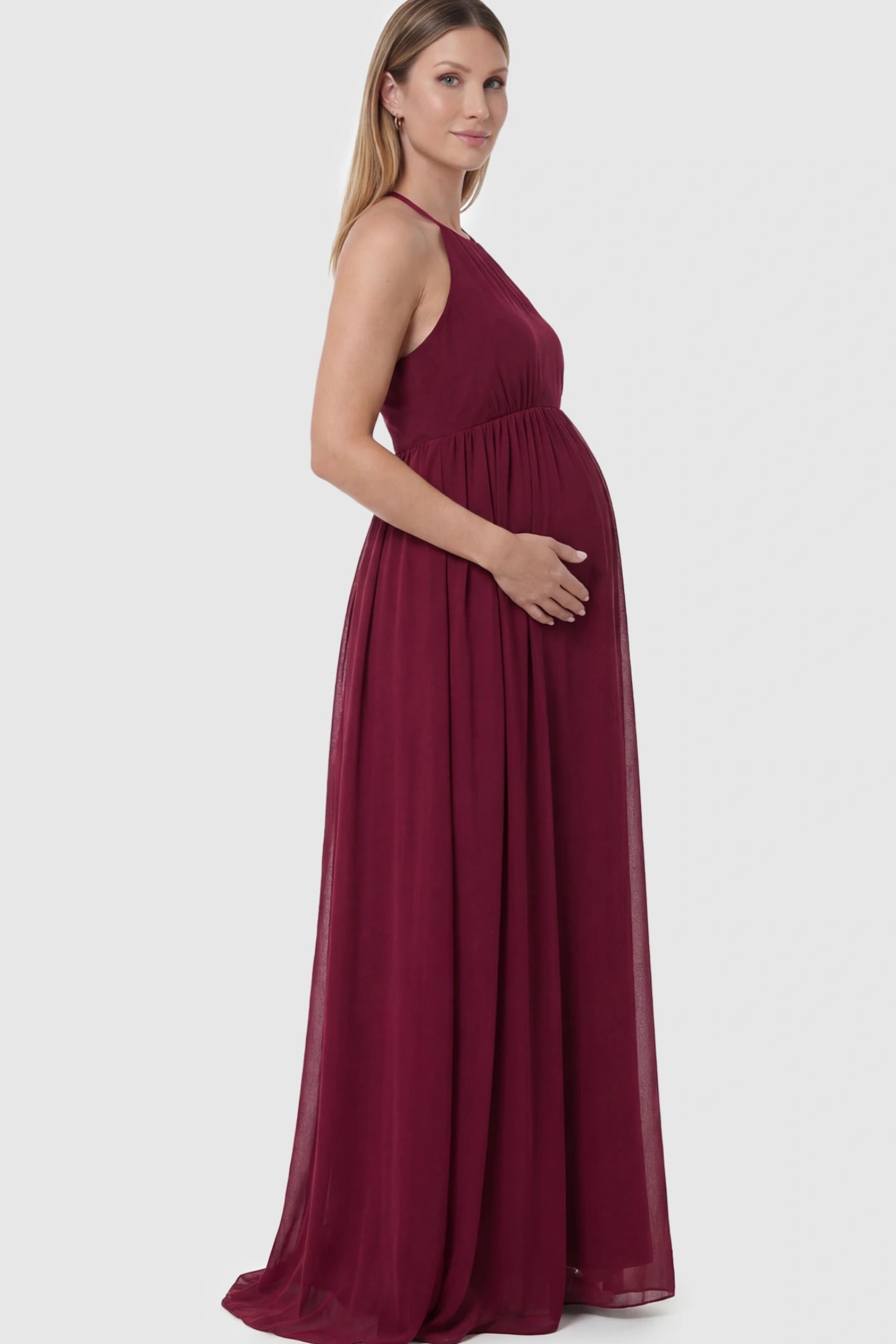Pleated Mesh Sleeveless Maternity Photoshoot Dress in Burgundy featuring a high-neckline and flowing skirt on a pregnant model.