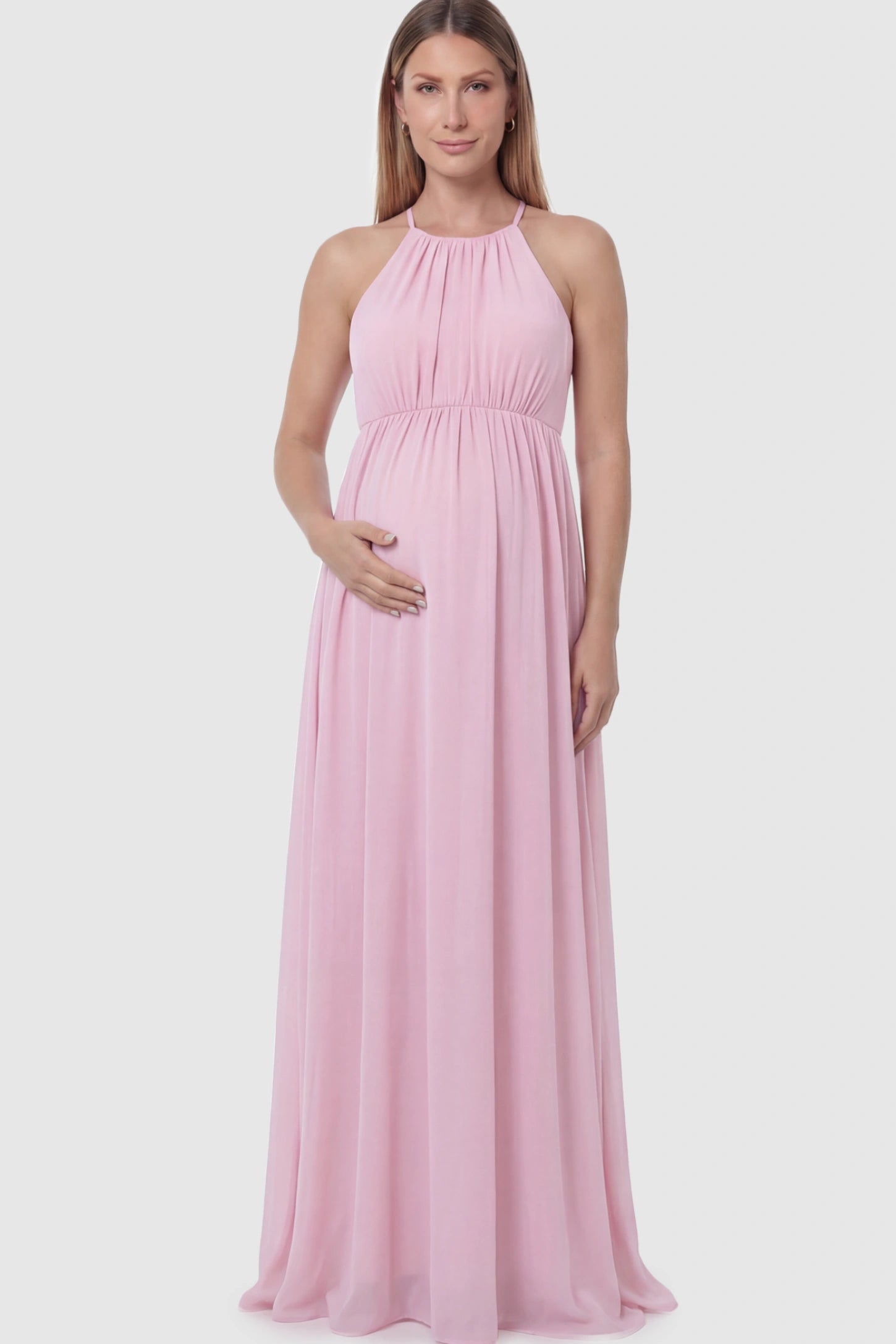 Pleated Mesh Sleeveless Maternity Photoshoot Dress Pleated Mesh Sleeveless Maternity Photoshoot Dress in Pink featuring a high-neckline and flowing skirt on a pregnant model.