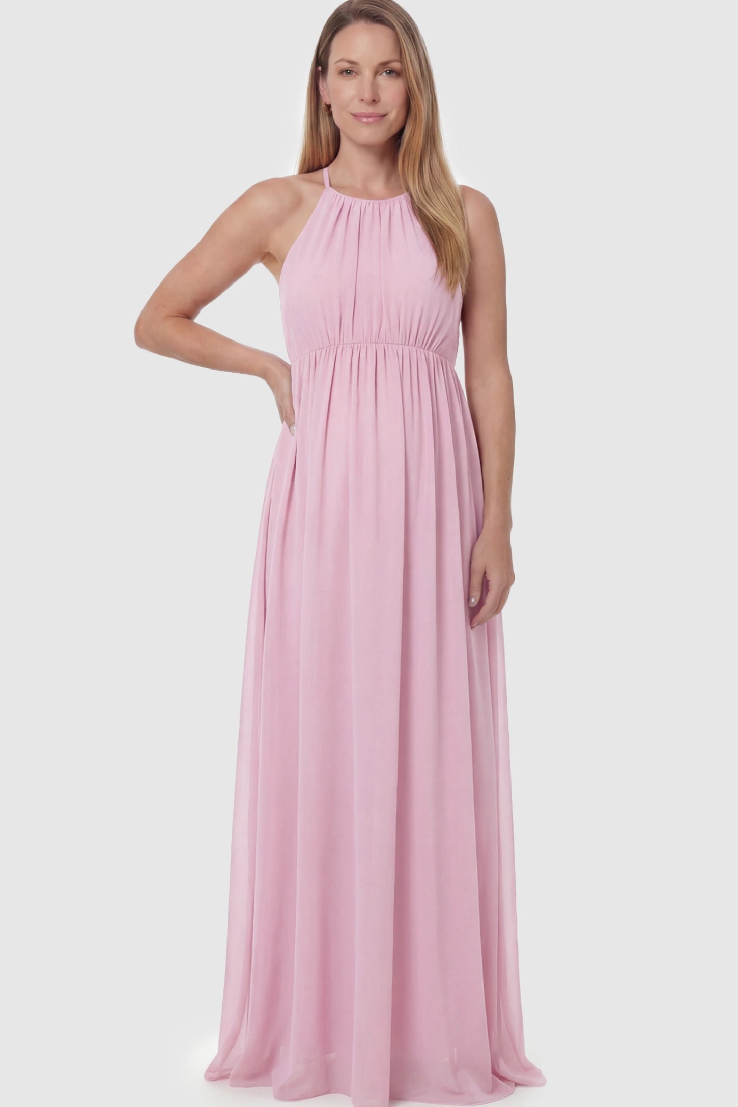 Pleated Mesh Sleeveless Maternity Photoshoot Dress Pleated Mesh Sleeveless Maternity Photoshoot Dress in Pink featuring a high-neckline and flowing skirt on a postpartum model.