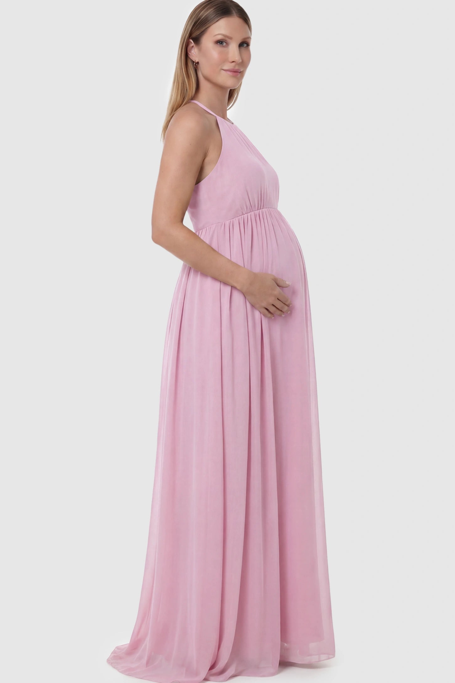 Pleated Mesh Sleeveless Maternity Photoshoot Dress Pleated Mesh Sleeveless Maternity Photoshoot Dress in Pink featuring a high-neckline and flowing skirt on a pregnant model.