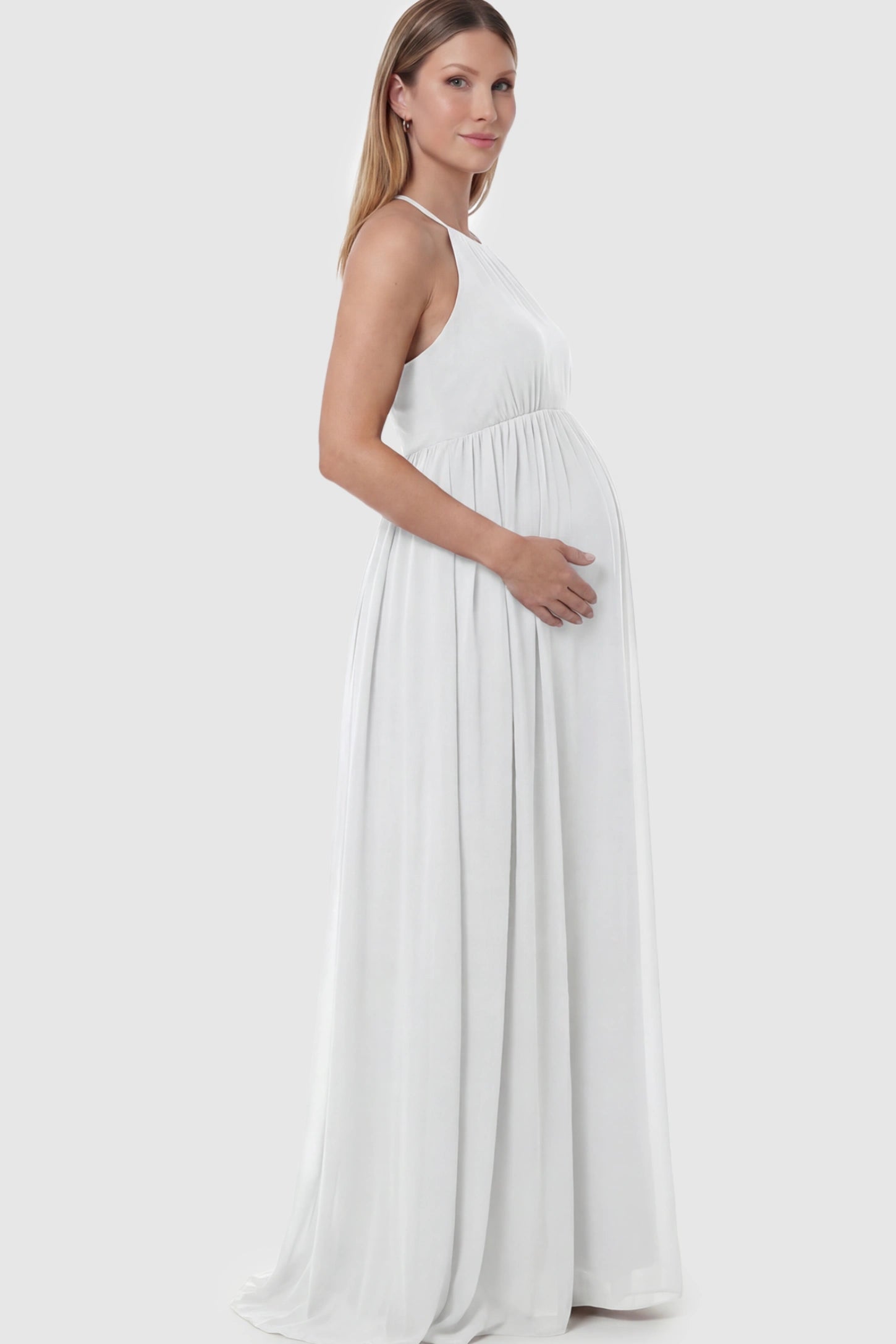 Pleated Mesh Sleeveless Maternity Photoshoot Dress Pleated Mesh Sleeveless Maternity Photoshoot Dress in White featuring a high-neckline and flowing skirt on a pregnant model.