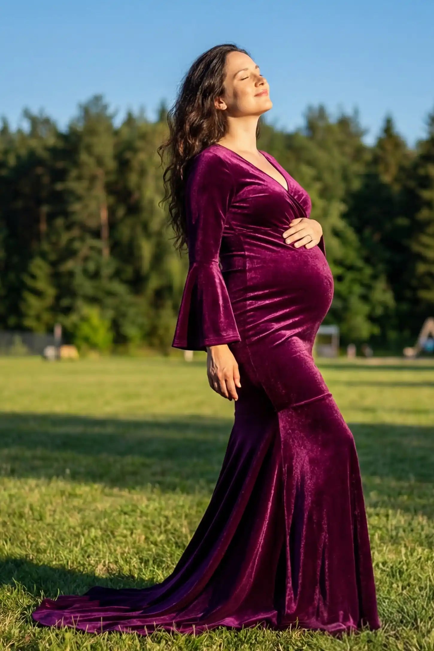 Side of Velvet Long Bell Sleeve Maternity Mermaid Gown in Burgundy featuring a curve-hugging silhouette on a pregnant model.