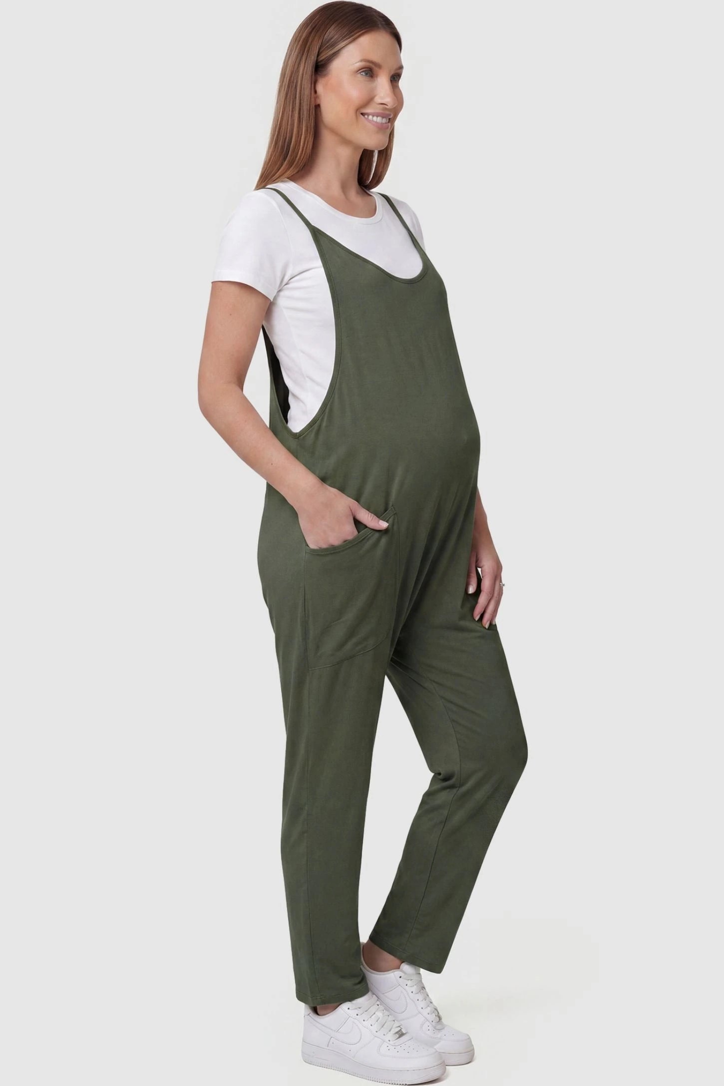 Adjustable Strap Pocketed Relaxed Maternity Jumpsuit Adjustable Strap Pocketed Maternity Jumpsuit in Army Green with functional side pockets on a pregnant model, side view.