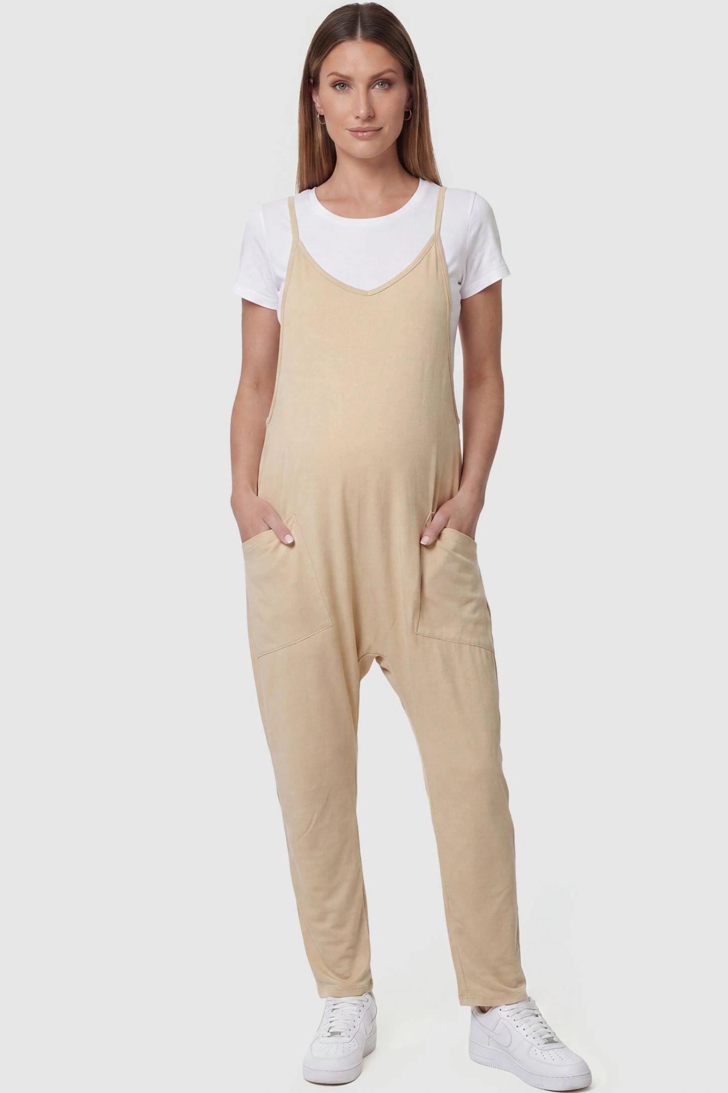 Adjustable Strap Pocketed Relaxed Maternity Jumpsuit Adjustable Strap Pocketed Maternity Jumpsuit in Beige featuring a relaxed fit on a pregnant model, front view.