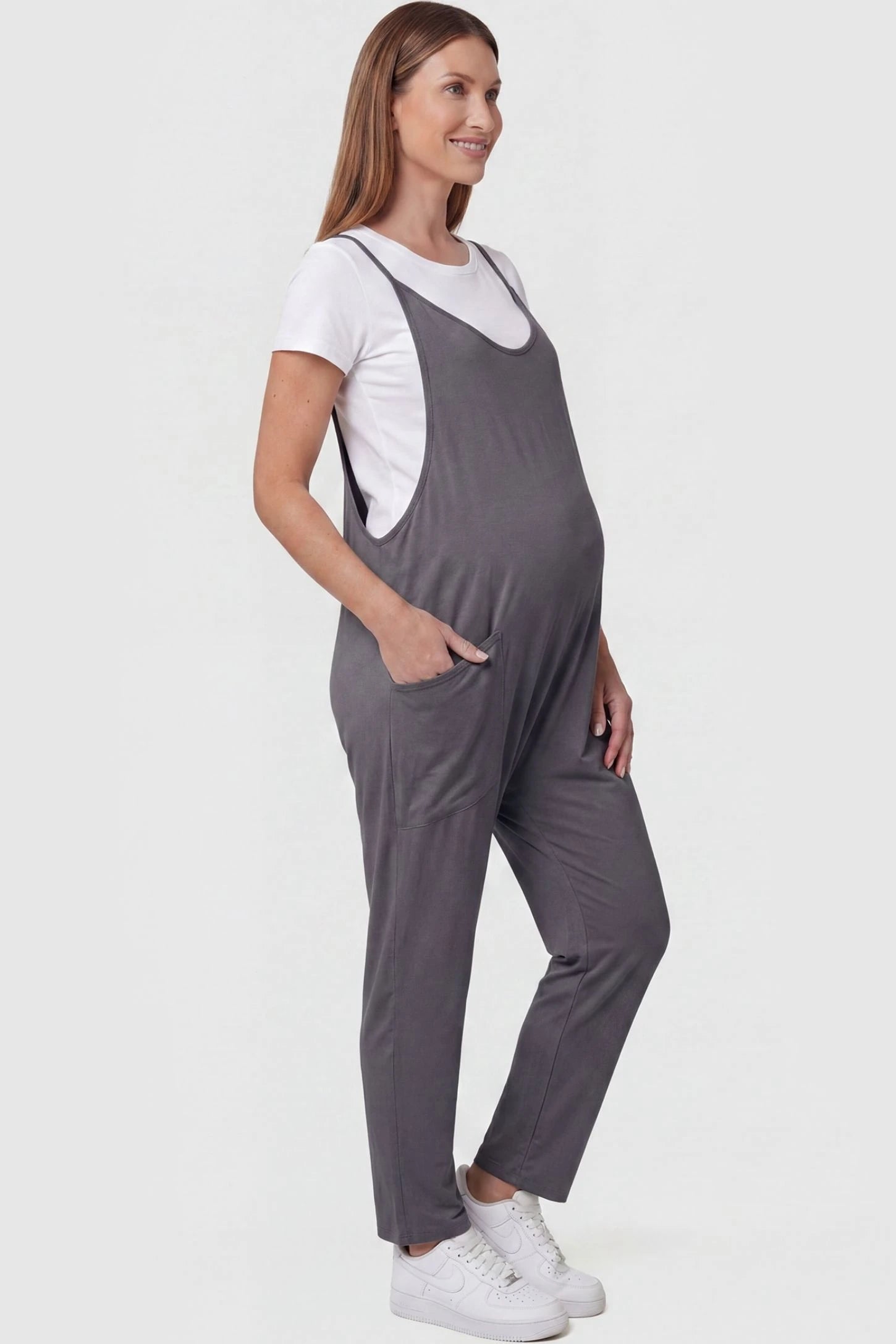 Adjustable Strap Pocketed Relaxed Maternity Jumpsuit Adjustable Strap Pocketed Maternity Jumpsuit in Dark Gray with functional side pockets on a pregnant model, side view.