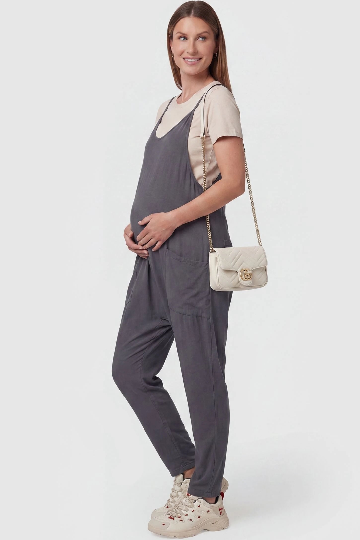 Adjustable Strap Pocketed Maternity Jumpsuit in Dark Gray with functional side pockets on a pregnant model, side view.