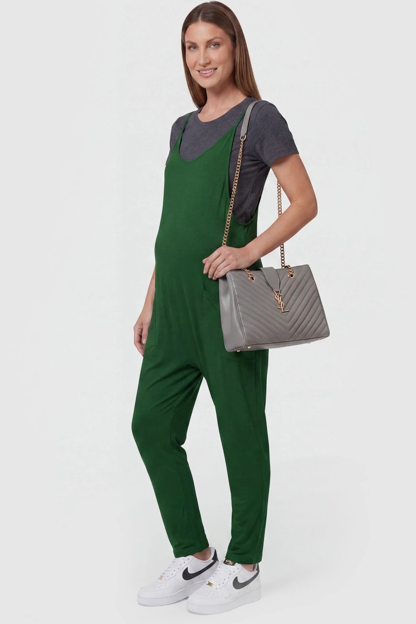 Adjustable Strap Pocketed Relaxed Maternity Jumpsuit Adjustable Strap Pocketed Maternity Jumpsuit in Dark Green with functional side pockets on a pregnant model, side view.