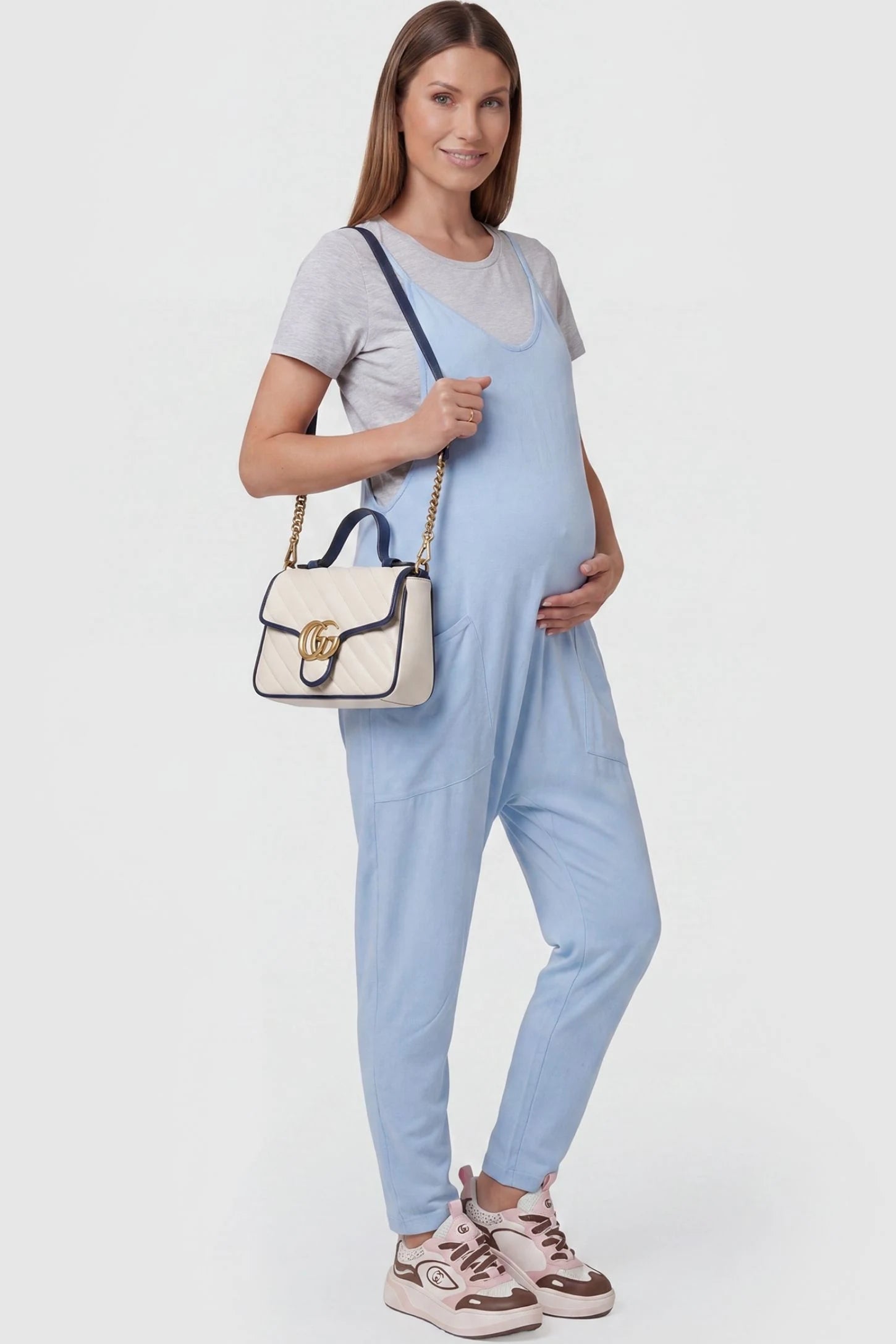 Adjustable Strap Pocketed Relaxed Maternity Jumpsuit Adjustable Strap Pocketed Maternity Jumpsuit in Light Blue with functional side pockets on a pregnant model, side view.