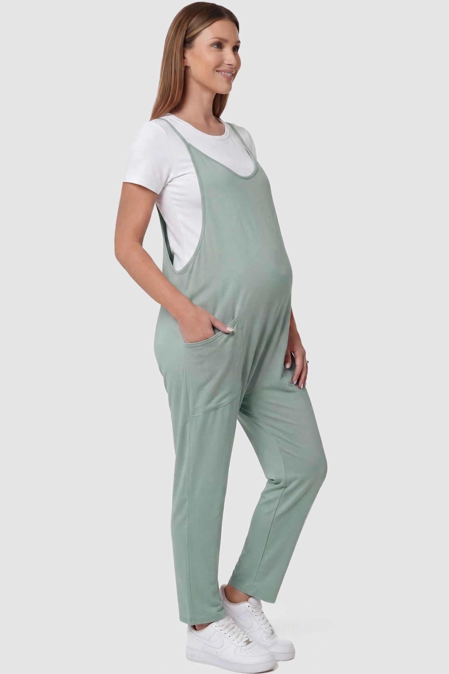 Adjustable Strap Pocketed Relaxed Maternity Jumpsuit Adjustable Strap Pocketed Maternity Jumpsuit in Light Green with functional side pockets on a pregnant model, side view.