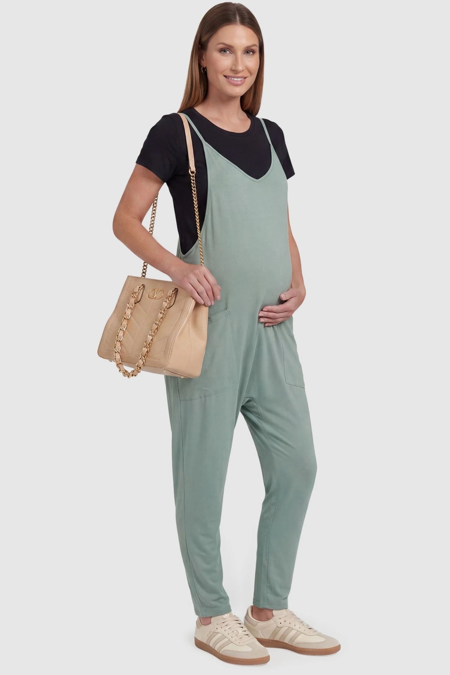 Adjustable Strap Pocketed Relaxed Maternity Jumpsuit Adjustable Strap Pocketed Maternity Jumpsuit in Light Green with functional side pockets on a pregnant model, side view.