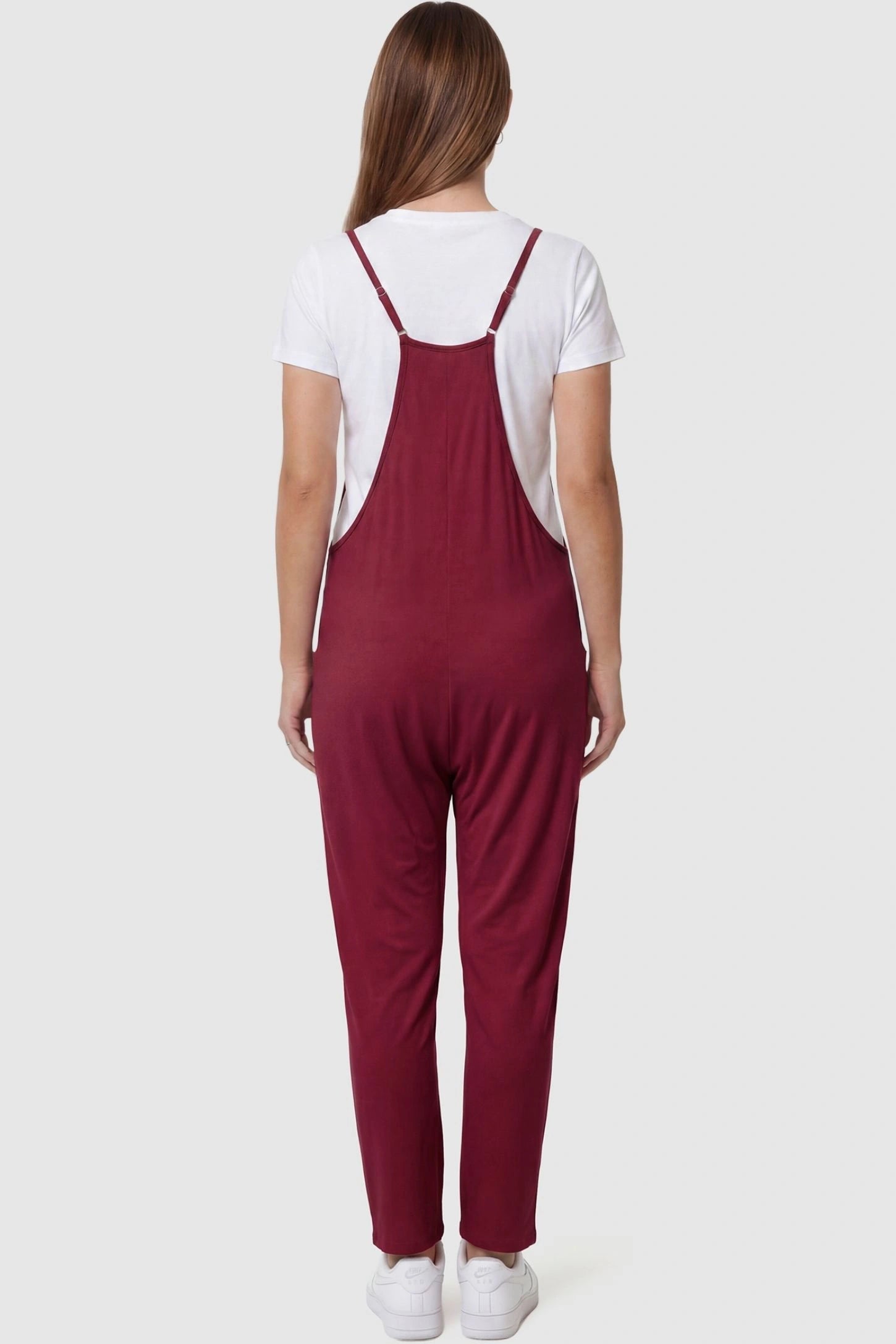 Adjustable Strap Pocketed Relaxed Maternity Jumpsuit Adjustable Strap Pocketed Maternity Jumpsuit in Wine Red featuring adjustable shoulder straps on a pregnant model, back view.