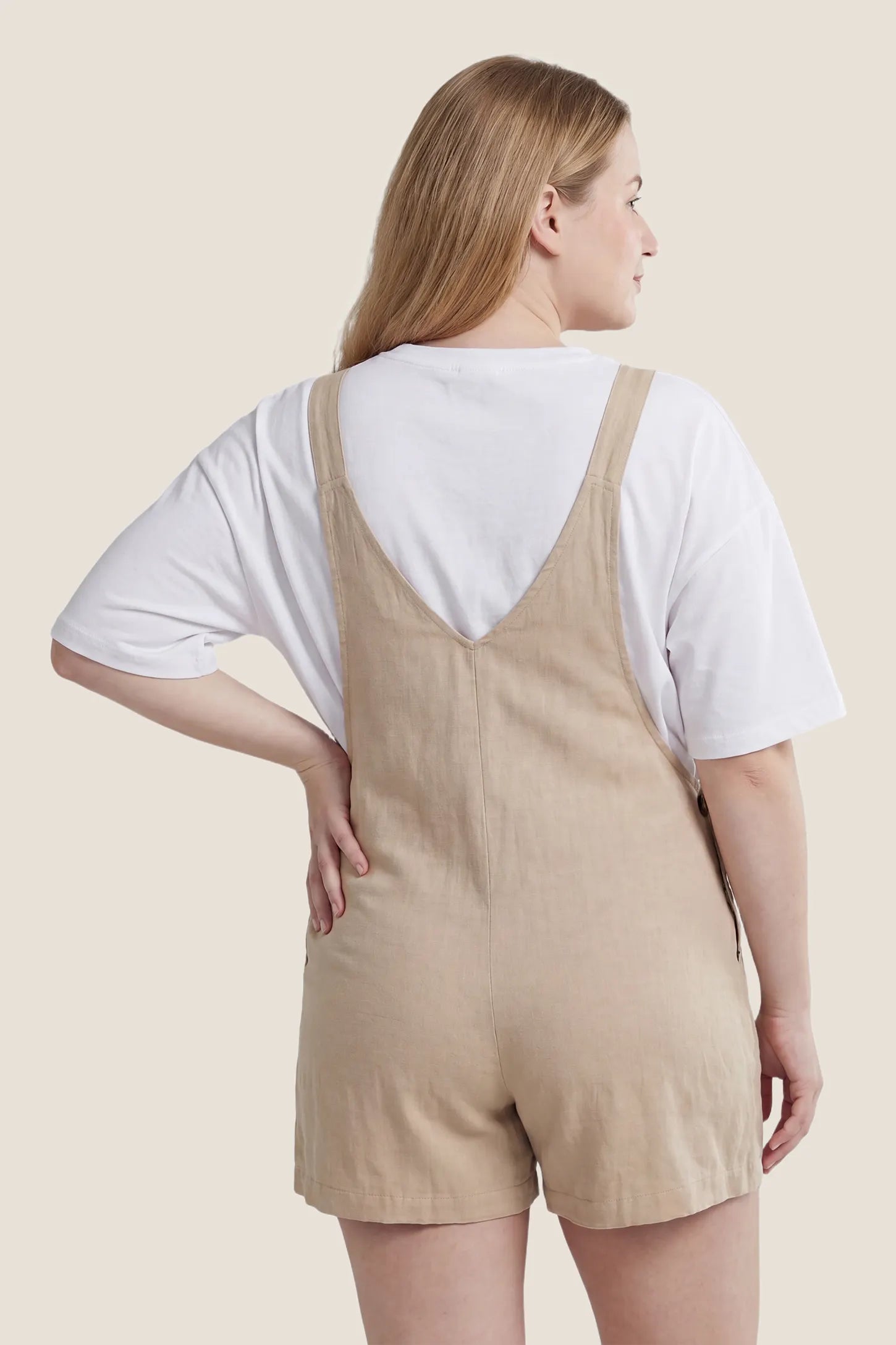 Adjustable Waist Pocketed Maternity Short Overalls Back view of the beige Adjustable Waist Pocketed Maternity Short Overalls with adjustable straps and a relaxed fit.
