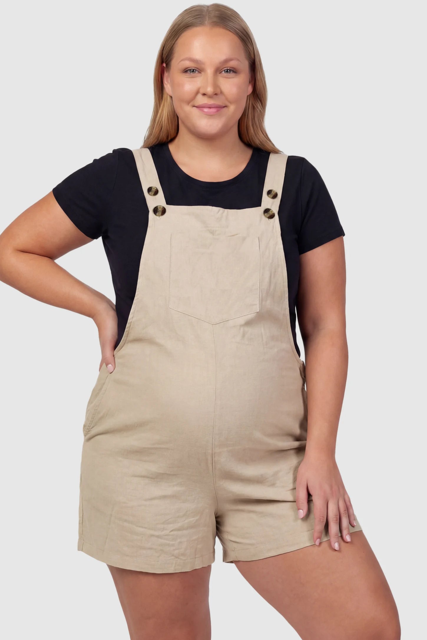 Adjustable Waist Pocketed Maternity Short Overalls Adjustable Waist Pocketed Maternity Short Overalls in Beige featuring a bib pocket on a plus size pregnant model, front view.