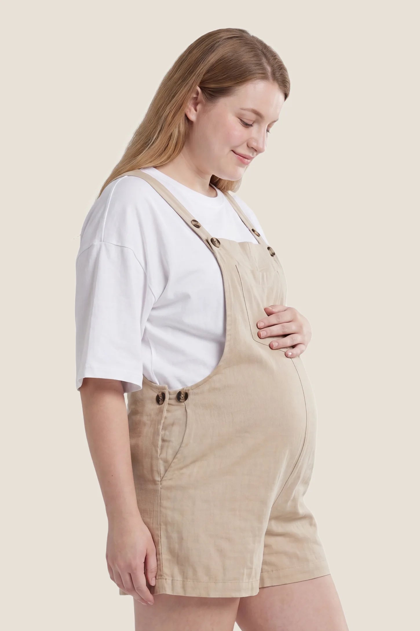 Adjustable Waist Pocketed Maternity Short Overalls Side view of the beige Adjustable Waist Pocketed Maternity Short Overalls designed to fit comfortably throughout pregnancy.