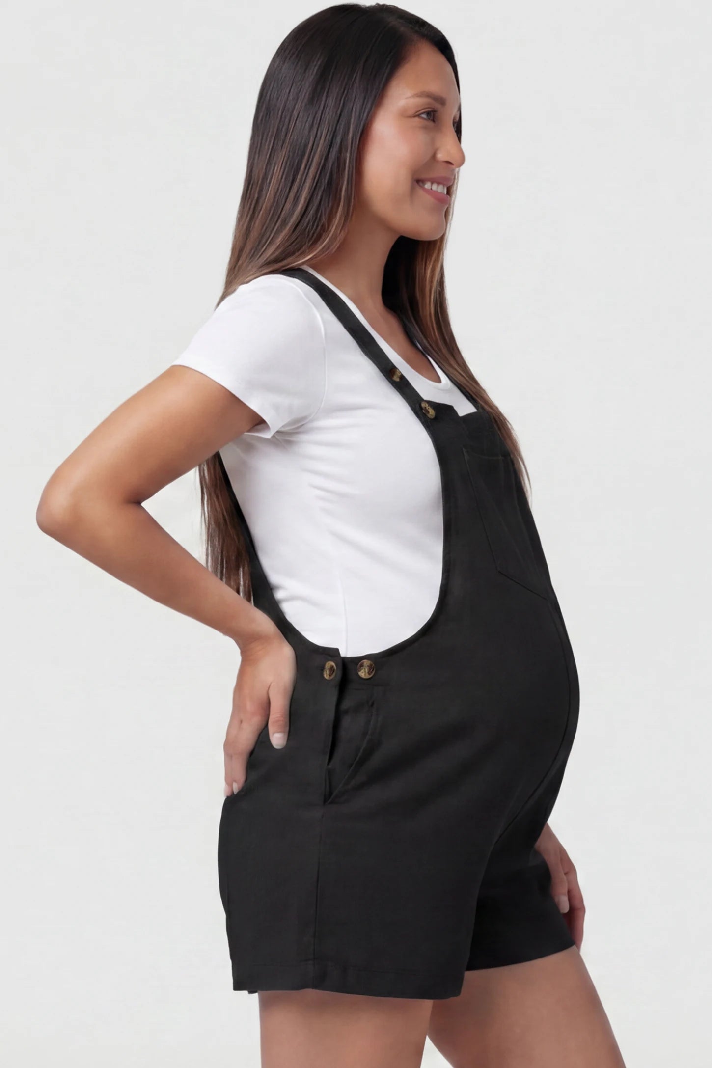Adjustable Waist Pocketed Maternity Short Overalls in Black featuring functional side buttons on a pregnant model, side view.