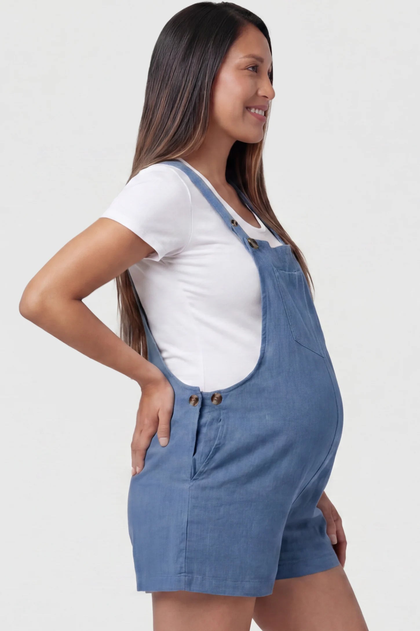 Adjustable Waist Pocketed Maternity Short Overalls Adjustable Waist Pocketed Maternity Short Overalls in Blue featuring functional side buttons on a pregnant model, side view.