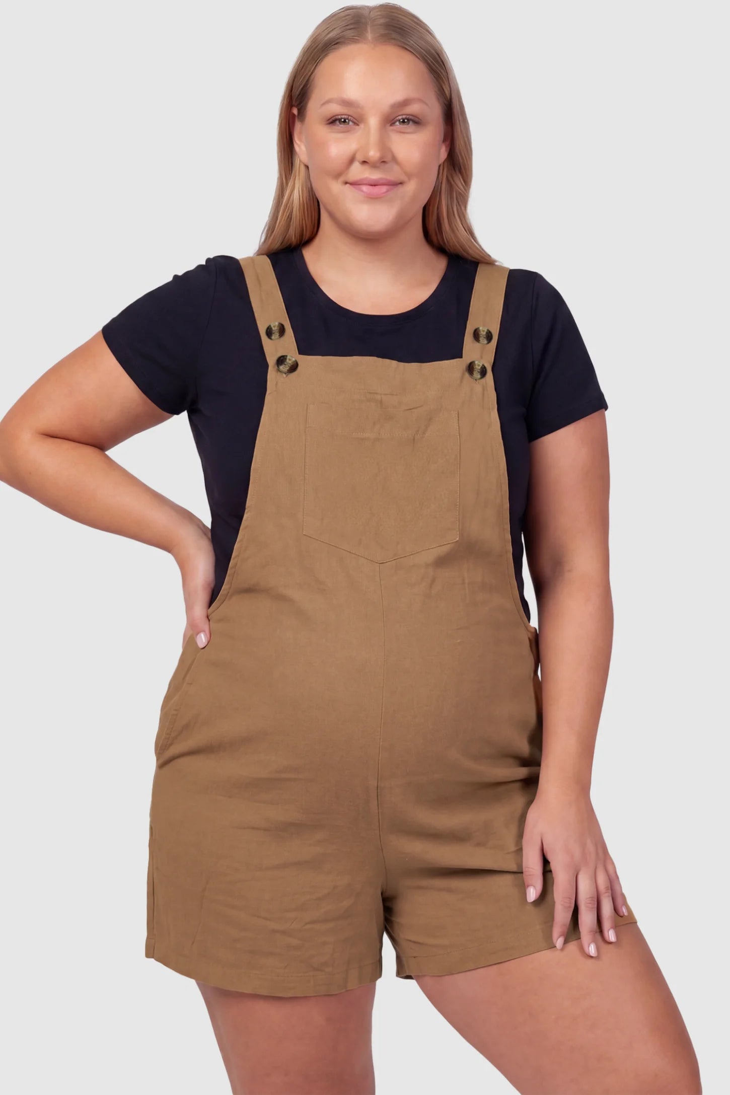 Adjustable Waist Pocketed Maternity Short Overalls Adjustable Waist Pocketed Maternity Short Overalls in Brown featuring a bib pocket on a plus size pregnant model, front view.