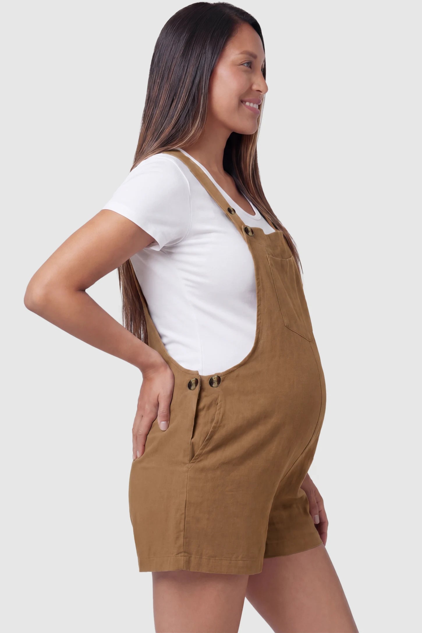 Adjustable Waist Pocketed Maternity Short Overalls Adjustable Waist Pocketed Maternity Short Overalls in Brown featuring functional side buttons on a pregnant model, side view.