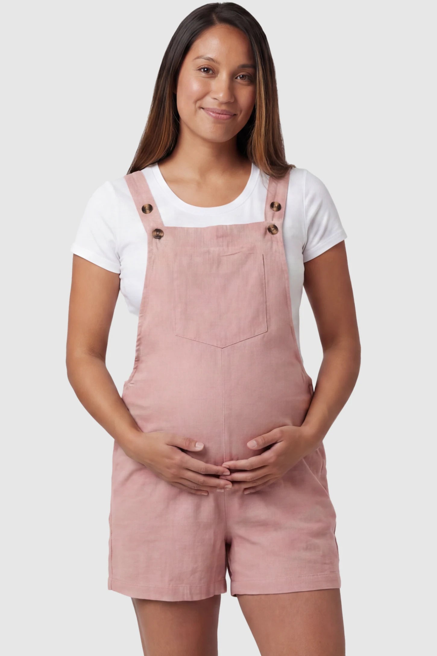 Adjustable Waist Pocketed Maternity Short Overalls Adjustable Waist Pocketed Maternity Short Overalls in Pink featuring a bib pocket on a pregnant model, front view.