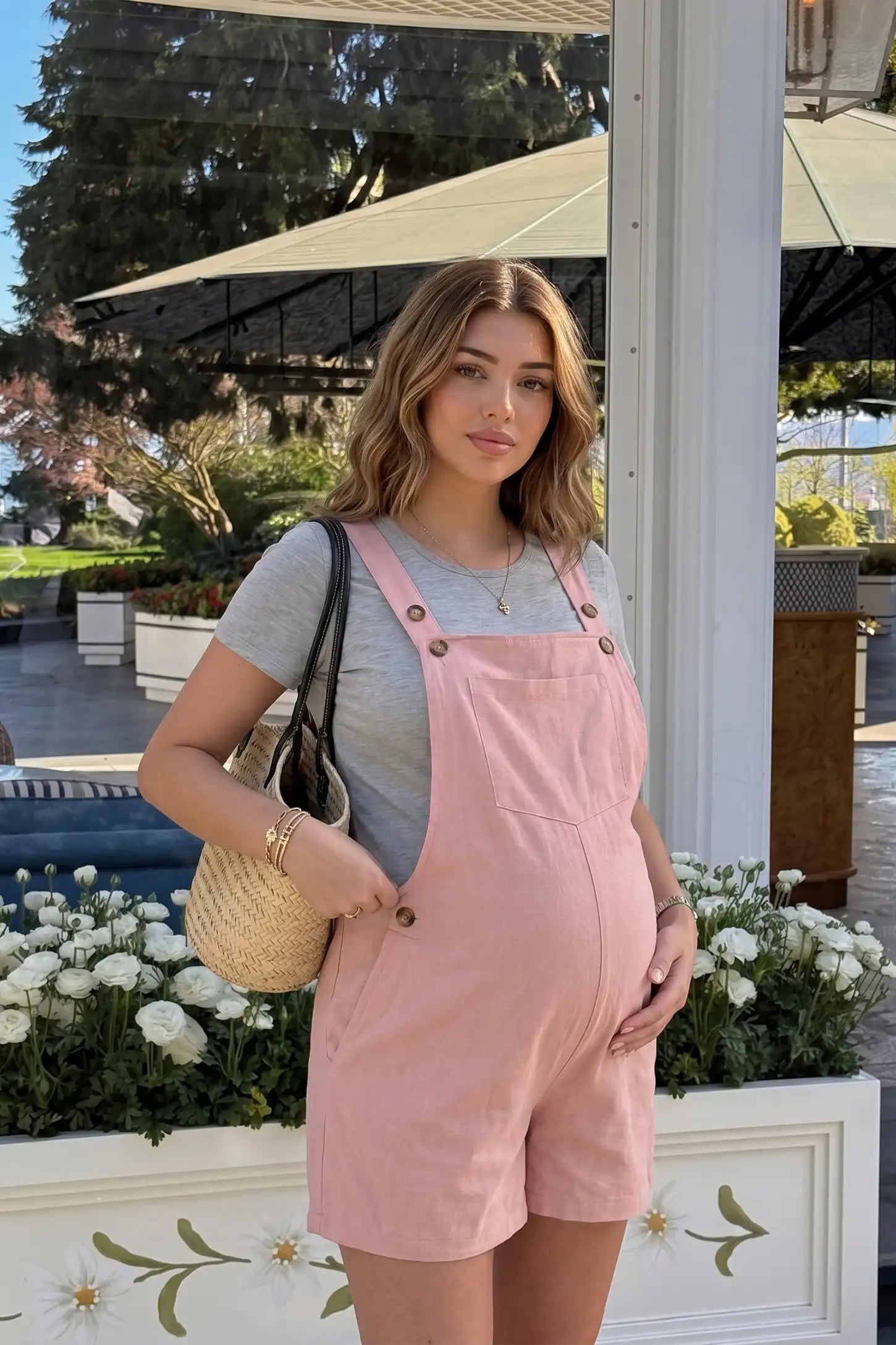 Outdoor lifestyle image of the pink Adjustable Waist Pocketed Maternity Short Overalls paired with a tee for an effortless summer look.