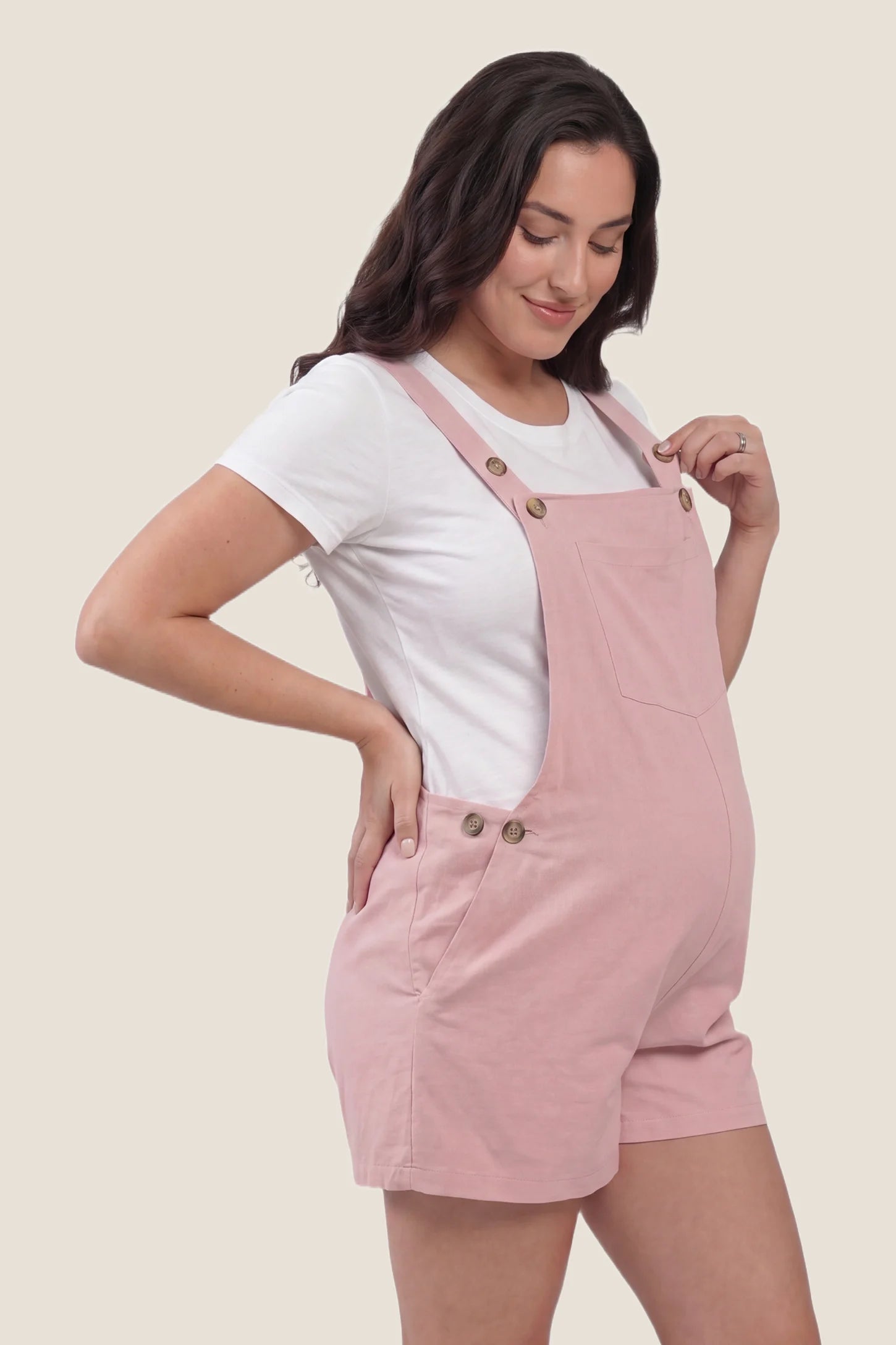 Adjustable Waist Pocketed Maternity Short Overalls Profile view of the pink Adjustable Waist Pocketed Maternity Short Overalls showing the relaxed silhouette and adjustable waist design.
