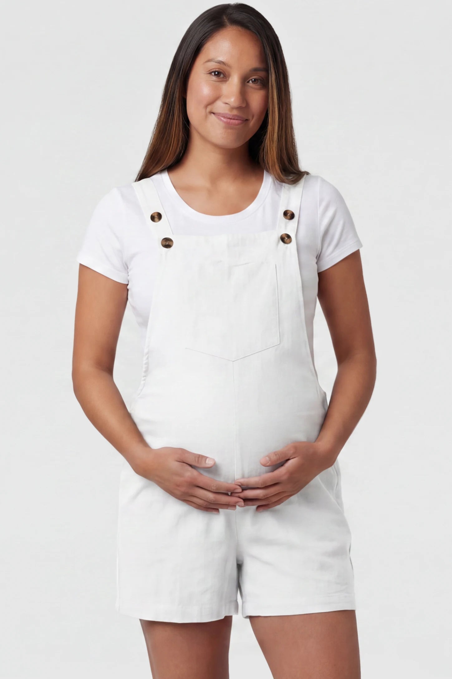 Adjustable Waist Pocketed Maternity Short Overalls Adjustable Waist Pocketed Maternity Short Overalls in White featuring a bib pocket on a pregnant model, front view.