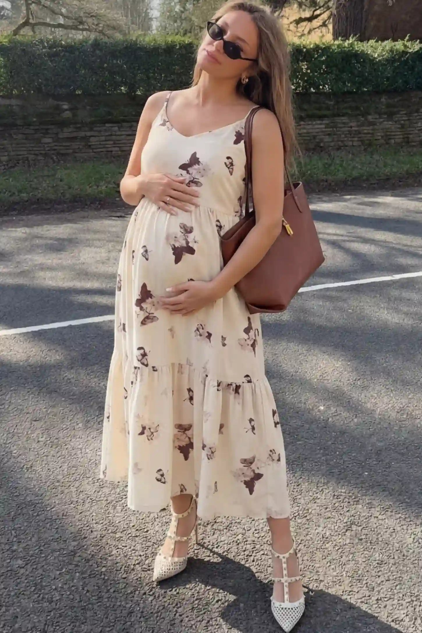 Butterfly Print V-Neck Tiered Maternity Midi Dress Butterfly Print Tiered Maternity Midi Dress in Beige Brown featuring a V-neckline and spaghetti straps on a pregnant woman.