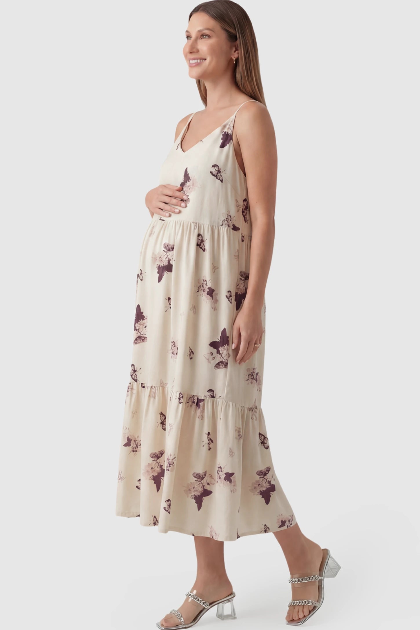 Butterfly Print V-Neck Tiered Maternity Midi Dress Butterfly Print Tiered Maternity Midi Dress in Beige Brown featuring a V-neckline and spaghetti straps on a pregnant model showing side.