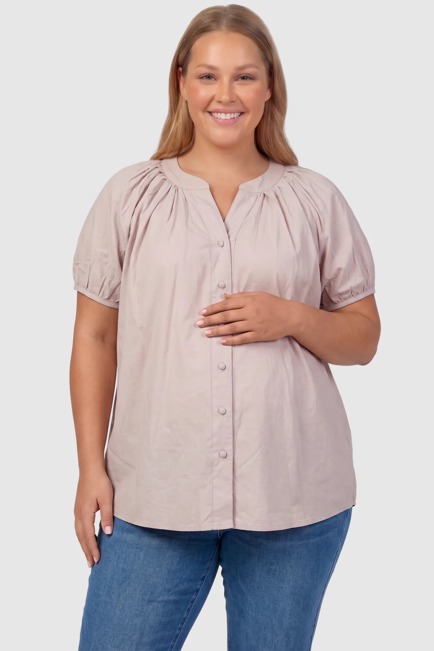 Button Front Short Sleeve Maternity Blouse Button Front Short Sleeve Maternity Blouse in Pink featuring gathered fabric and a button-up neck on a plus size pregnant model, front view.