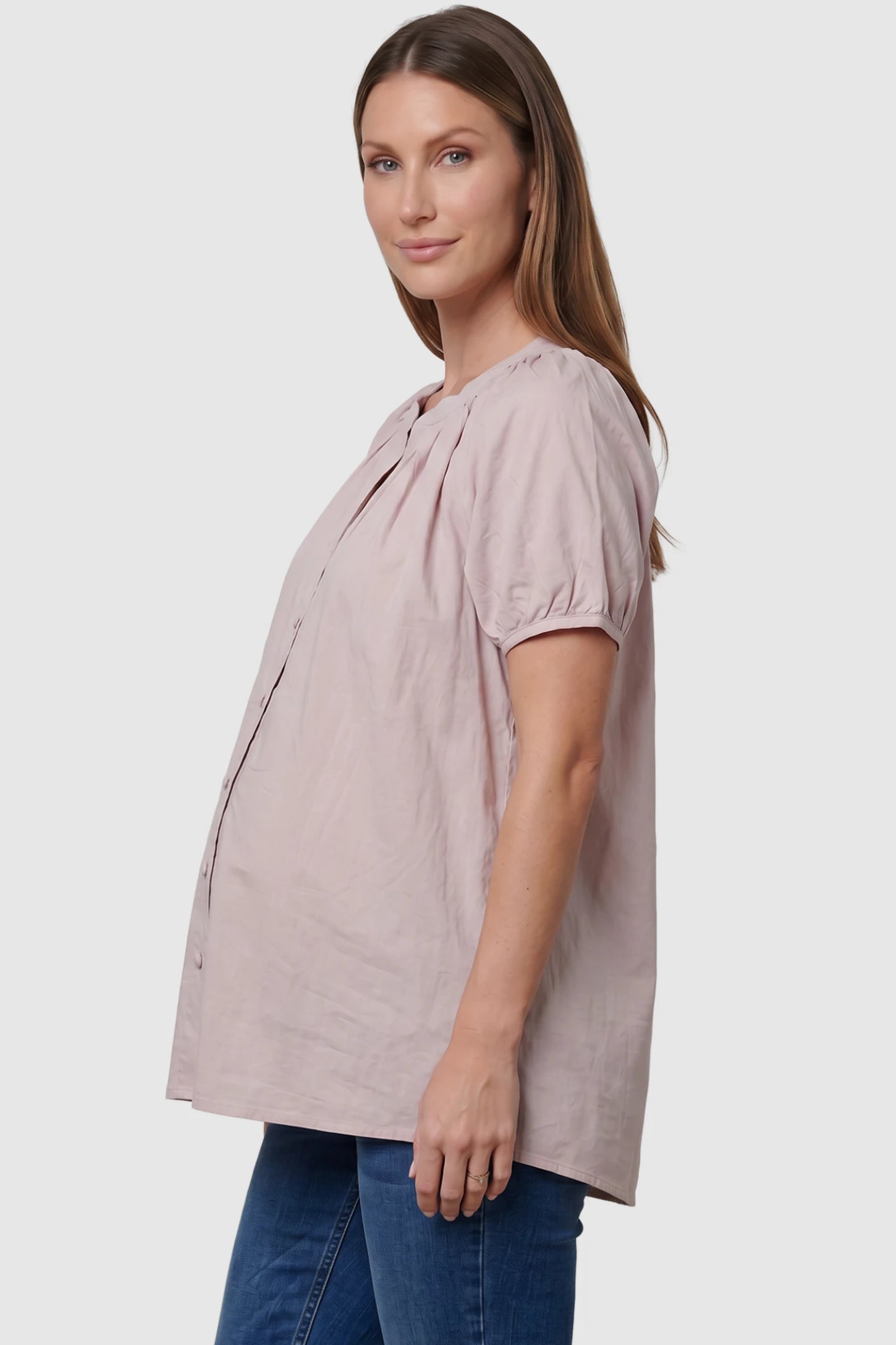 Button Front Short Sleeve Maternity Blouse in Pink featuring gathered fabric and a button-up neck on a pregnant model, side view.