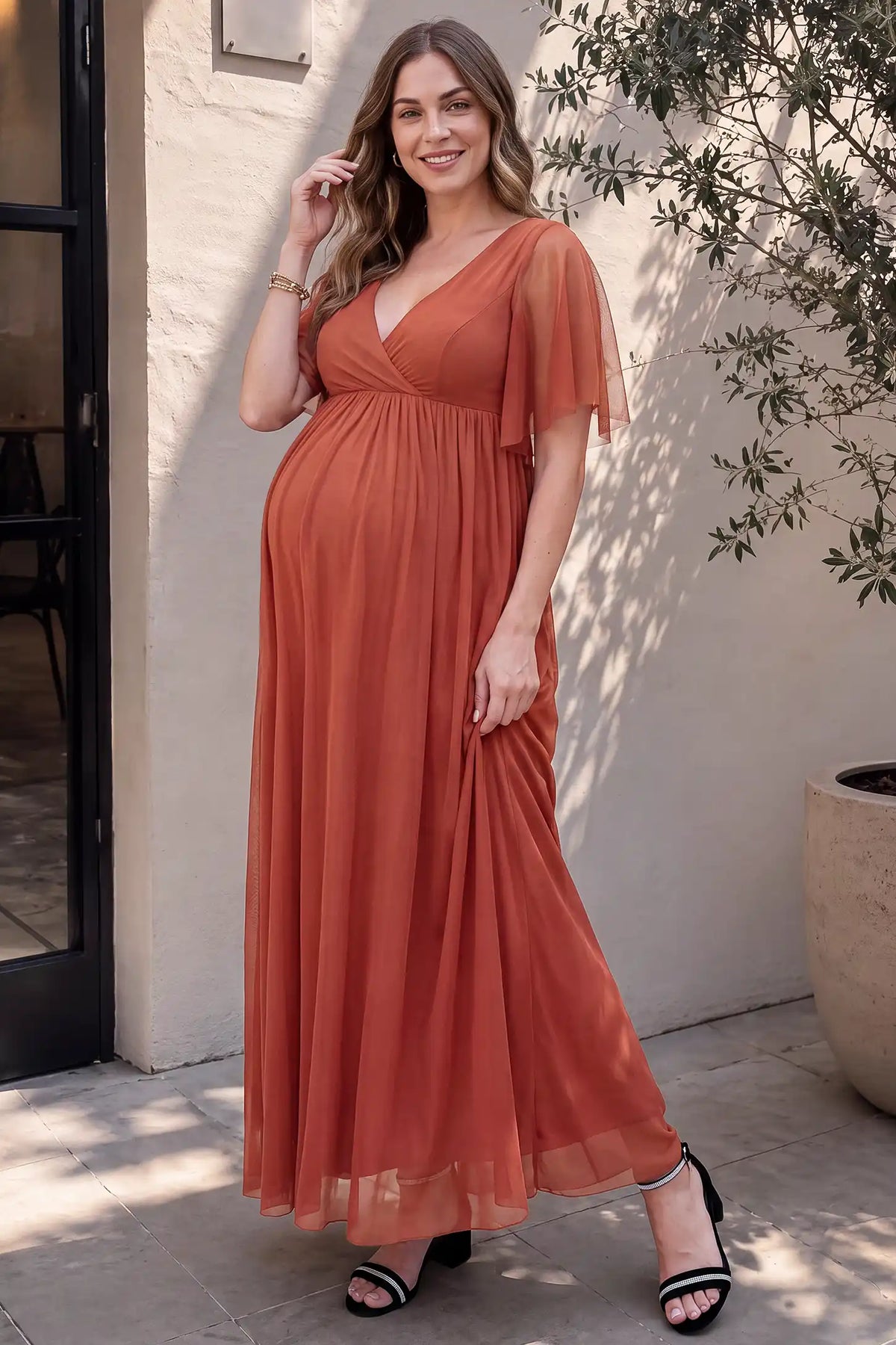 Chiffon Flutter Sleeve V-Neck Maternity Maxi Dress Chiffon Flutter Sleeve V-Neck Maternity Maxi Dress in Rust accommodating a growing bump on a pregnant model, studio side view.