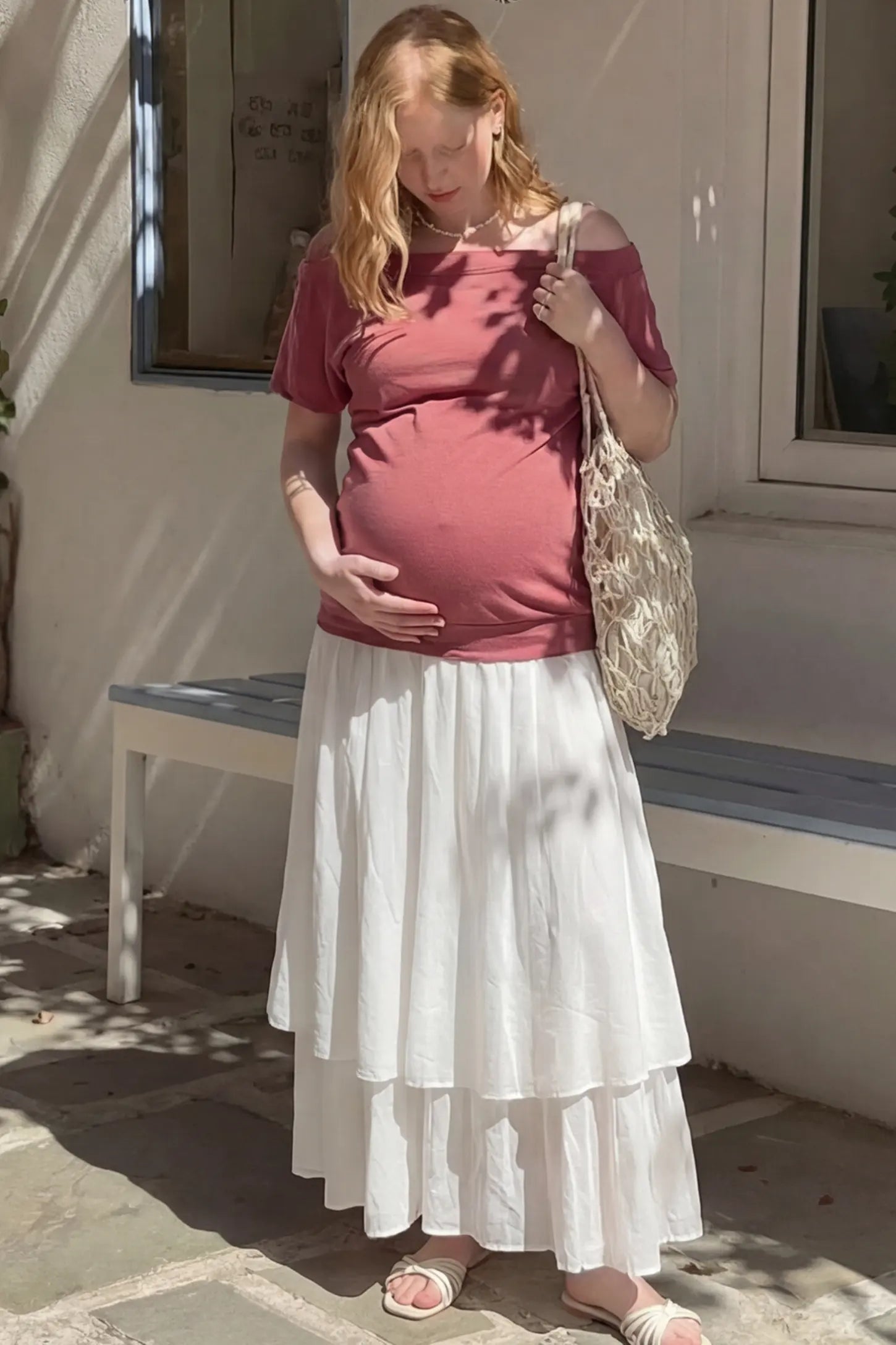 Convertible Neck Short Sleeve Maternity Top Convertible Neck Short Sleeve Maternity Top in pink featuring an adjustable neckline and a comfortable banded hem paired with white maxi skirt worn by a pregnant woman in an outdoor setting front view.