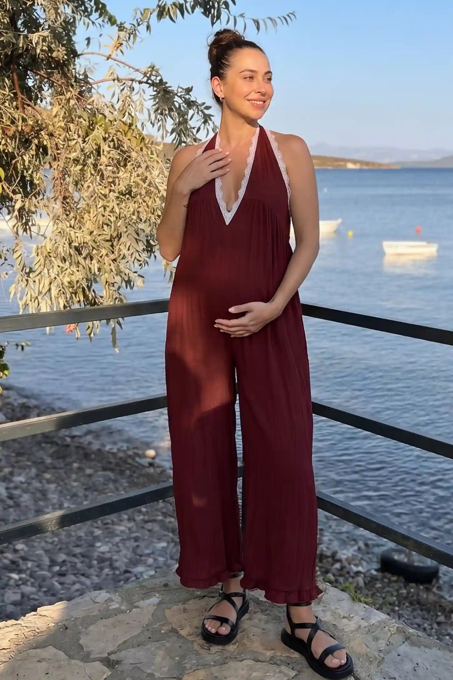 Deep V-Neck Lace Trim Wide Leg Maternity Jumpsuit Deep V-Neck Lace Trim Wide Leg Maternity Jumpsuit in Burgundy featuring an elegant deep V-neck and lace trim detail in an editorial lifestyle setting, pregnant model.