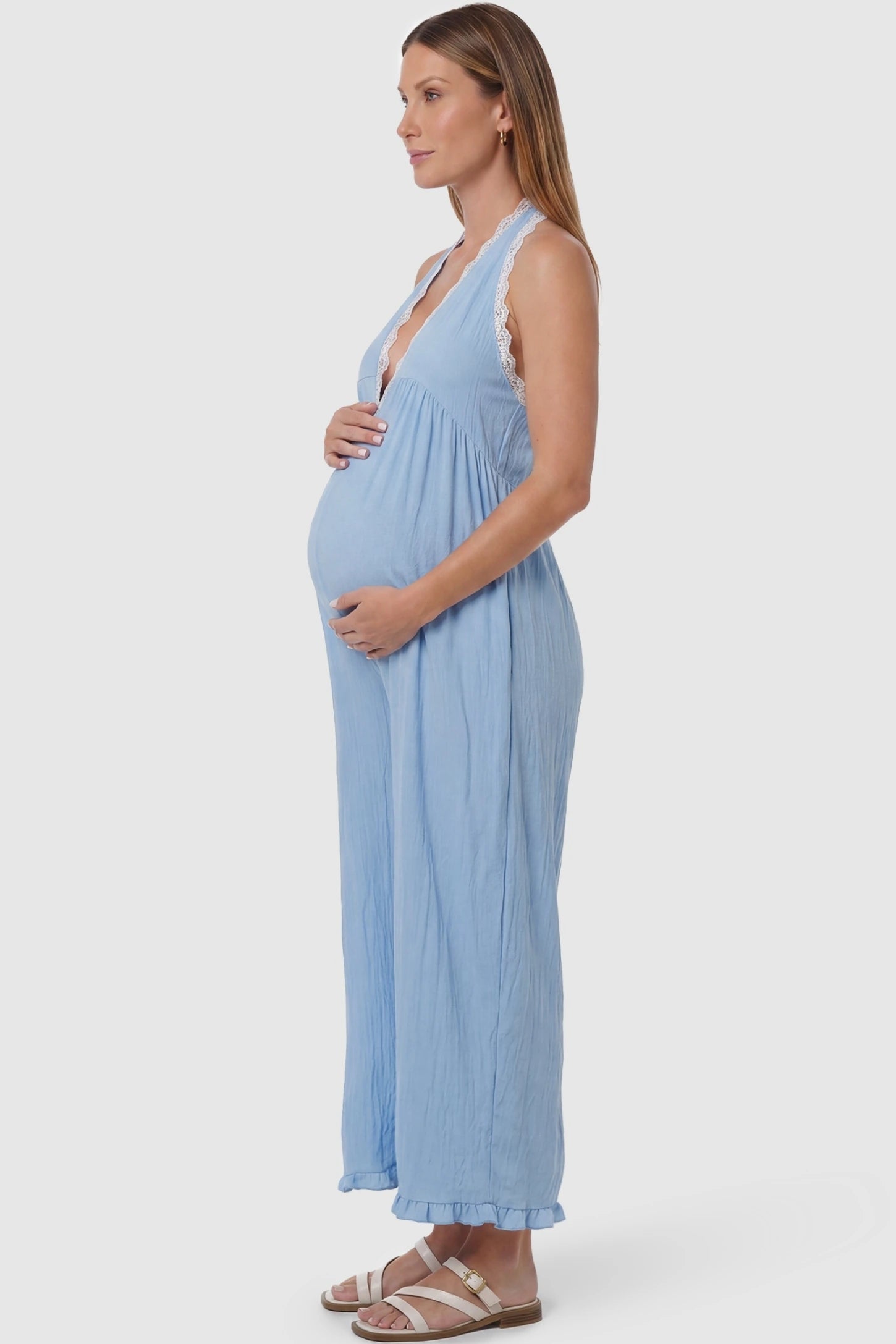 Deep V-Neck Lace Trim Wide Leg Maternity Jumpsuit Deep V-Neck Lace Trim Wide Leg Maternity Jumpsuit in Light Blue featuring a flowing wide leg silhouette on a pregnant model, side view.