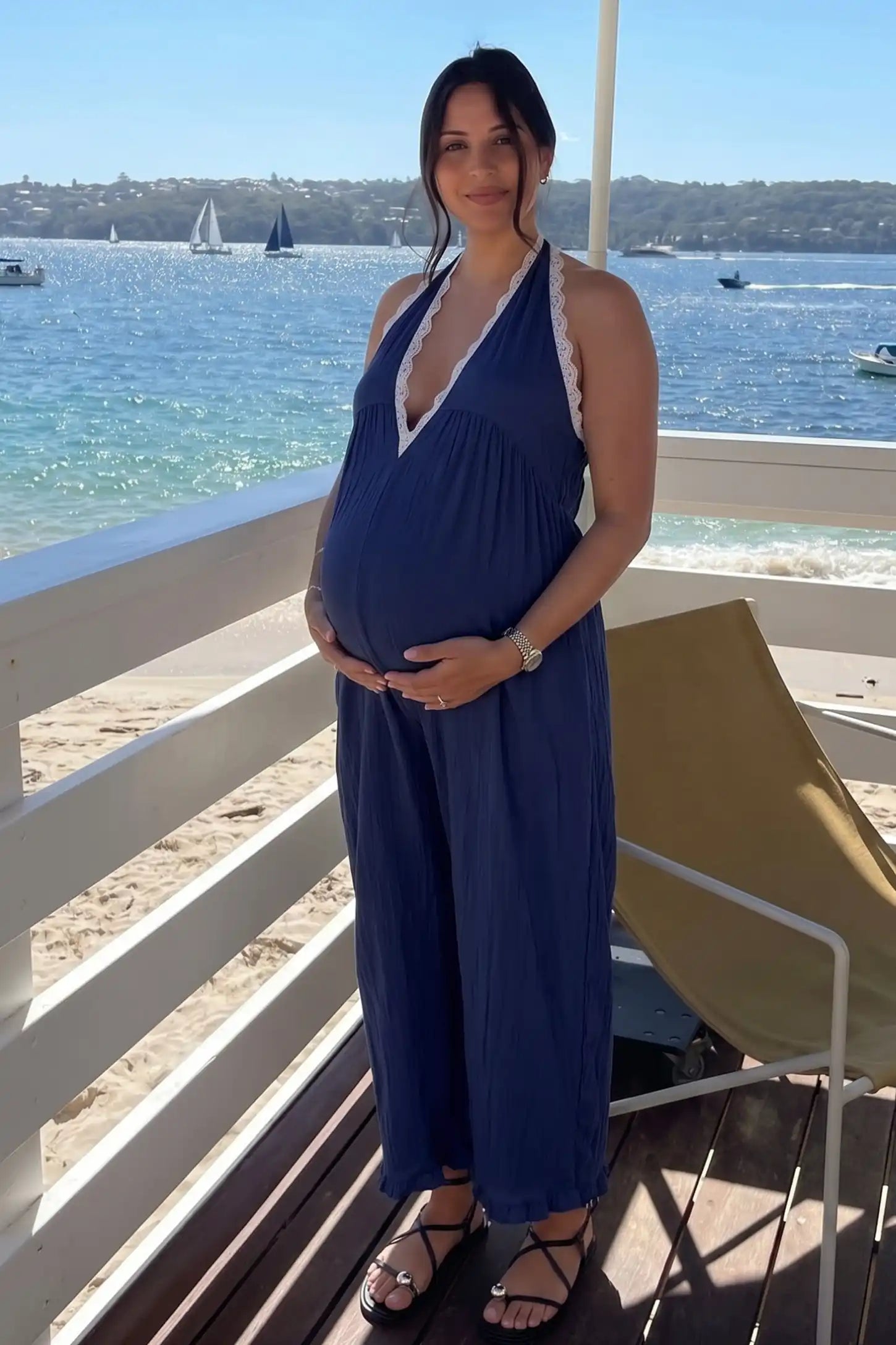 Deep V-Neck Lace Trim Wide Leg Maternity Jumpsuit Deep V-Neck Lace Trim Wide Leg Maternity Jumpsuit in Navy Blue featuring an elegant deep V-neck and lace trim detail in an editorial lifestyle setting, pregnant model.
