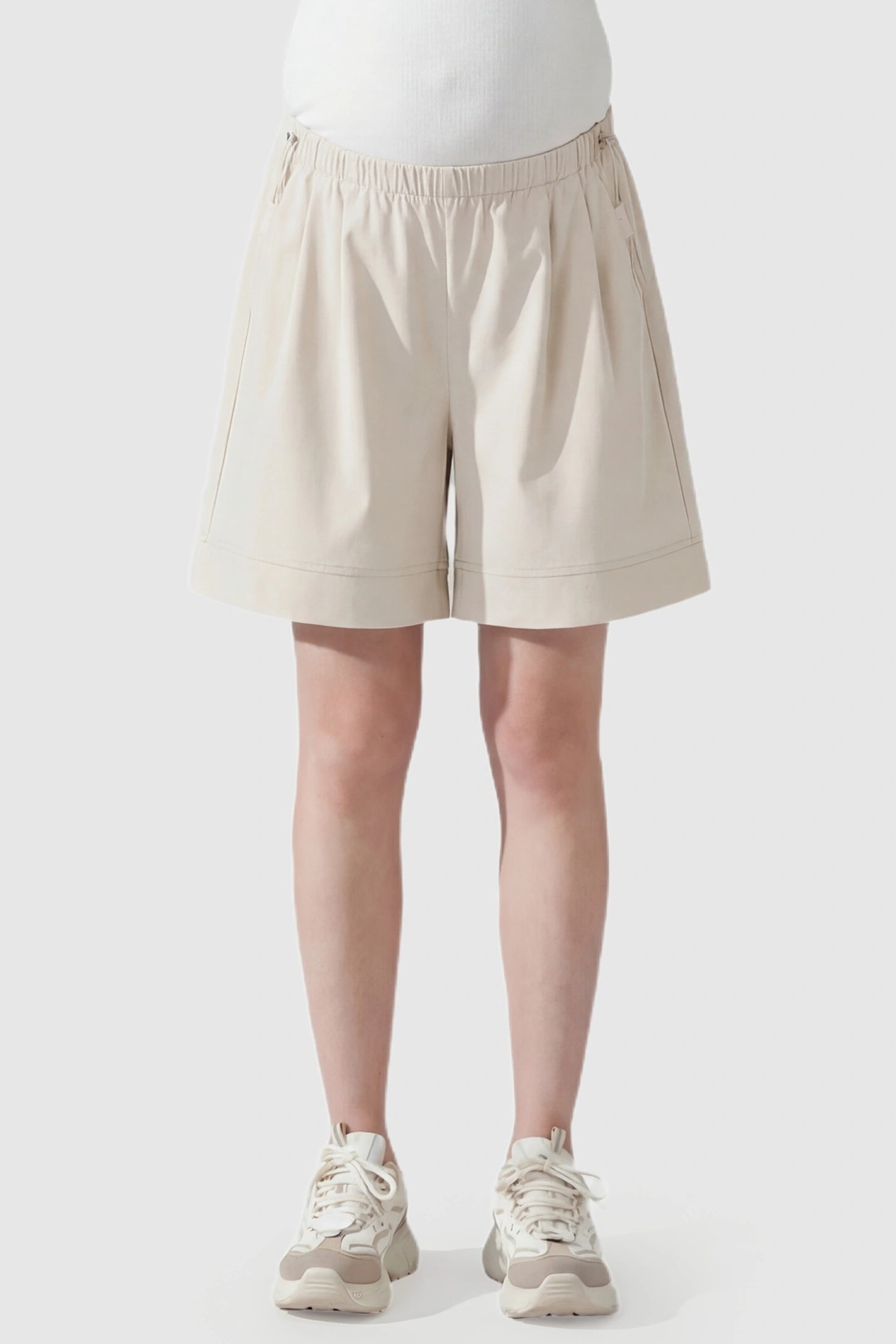 Pocketed Side Drawstring Maternity Shorts Beige Elasticated Waist Wide Leg Maternity Shorts featuring a flexible tummy band on a pregnant model, front view.