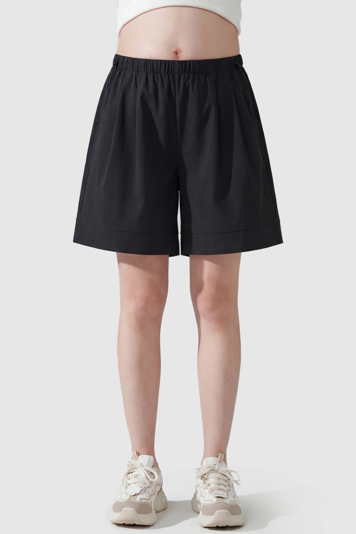 Pocketed Side Drawstring Maternity Shorts Black Elasticated Waist Soft Wide Leg Maternity Shorts featuring a supportive gathered waistband on a pregnant model, front view.