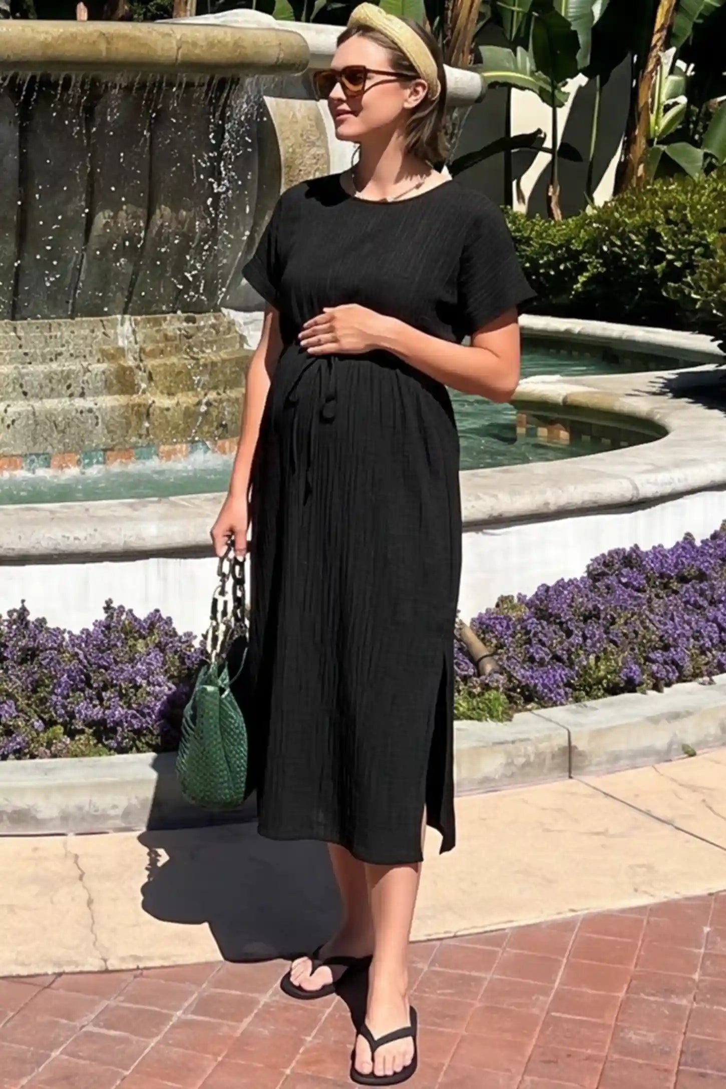Empire Waist Round Neck Maternity Midi Dress Empire Waist Round Neck Maternity Midi Dress in Black featuring elasticated waistband with a decorative tie detail on a plus size pregnant woman in outdoor setting, front view.