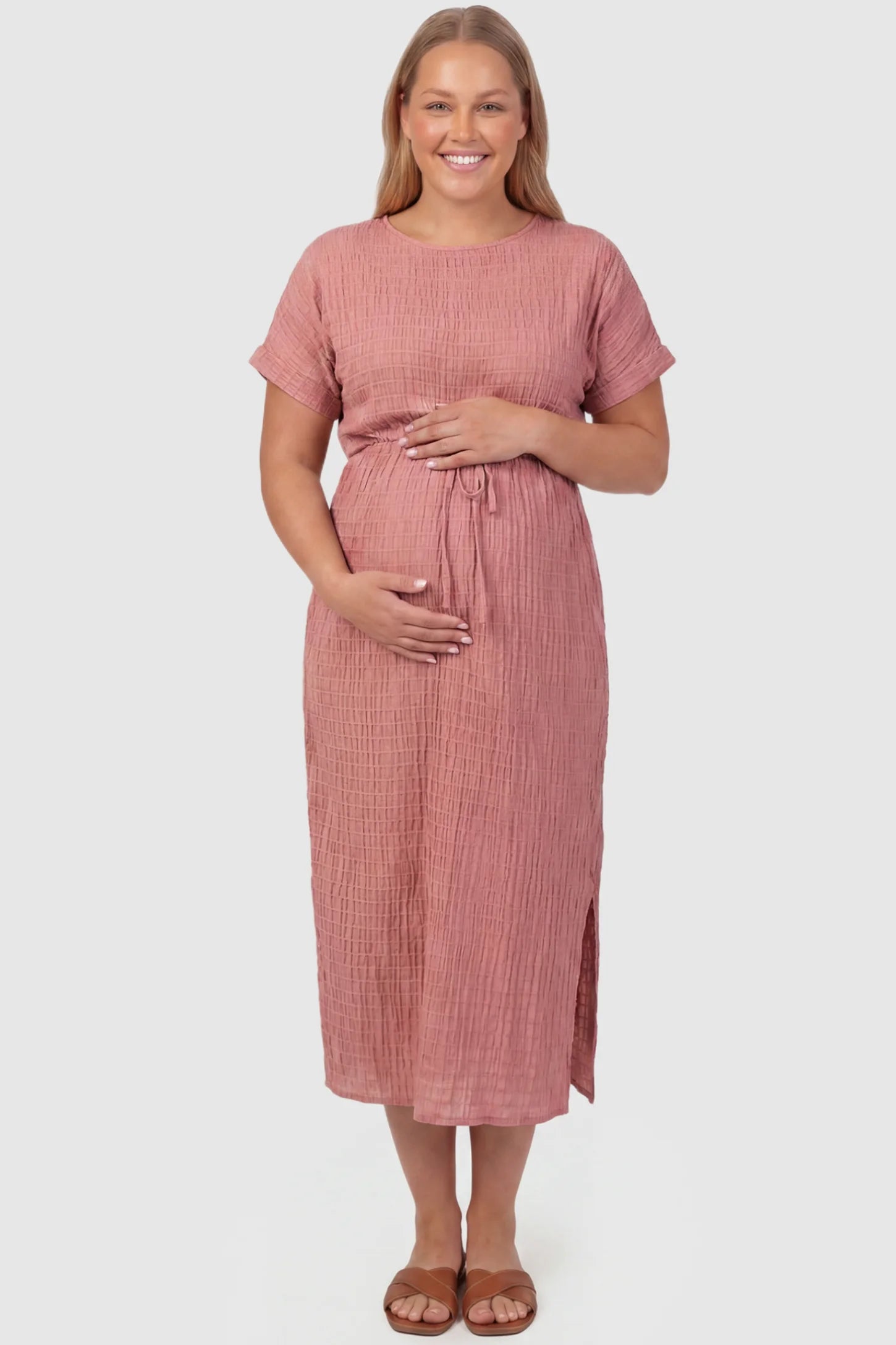 Empire Waist Round Neck Maternity Midi Dress Empire Waist Round Neck Maternity Midi Dress in Pink featuring elasticated waistband with a decorative tie detail on a plus size pregnant model, front view.