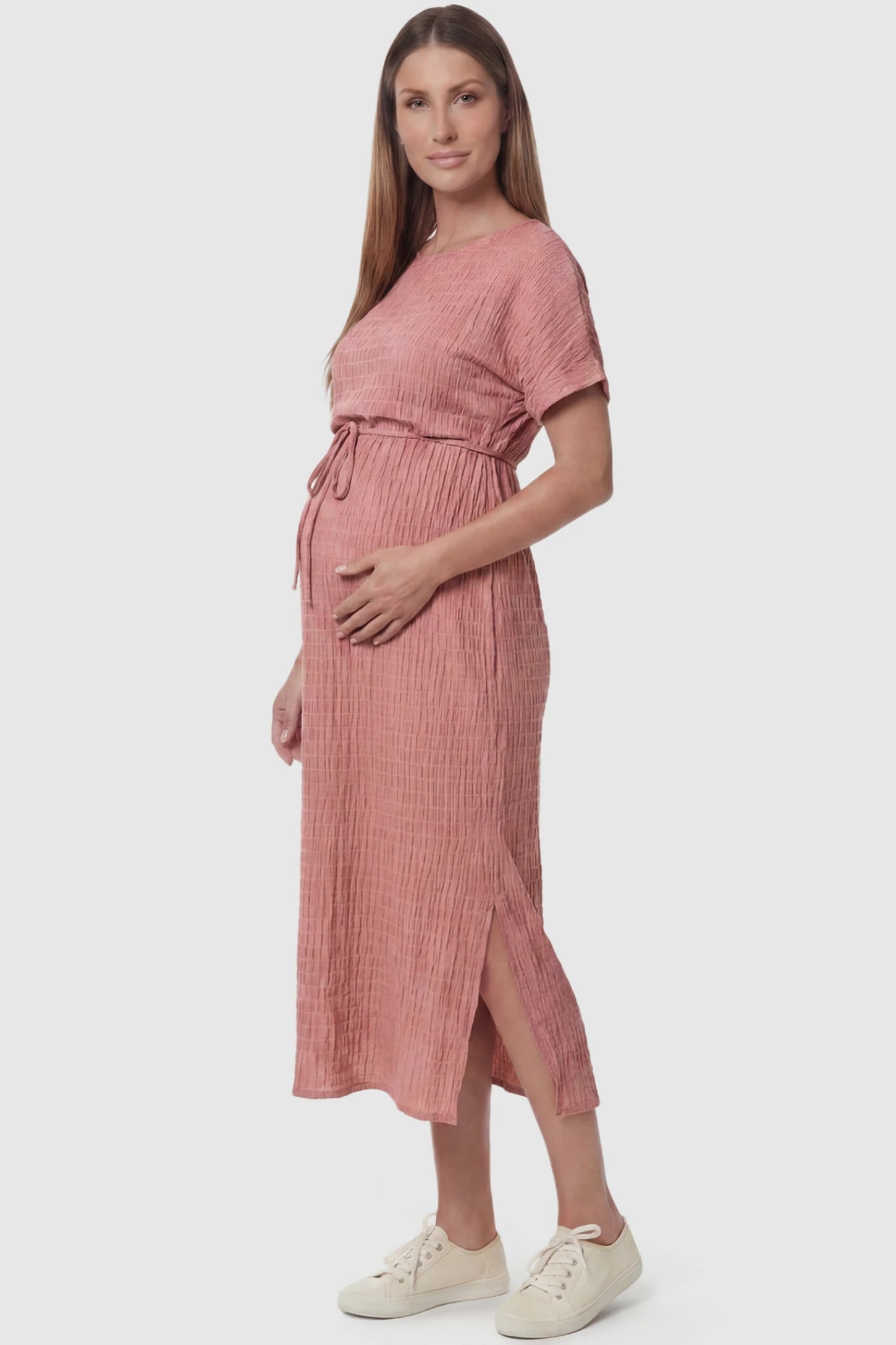 Empire Waist Round Neck Maternity Midi Dress Empire Waist Round Neck Maternity Midi Dress in Pink featuring elasticated waistband with a decorative tie detail on a pregnant model, side view.